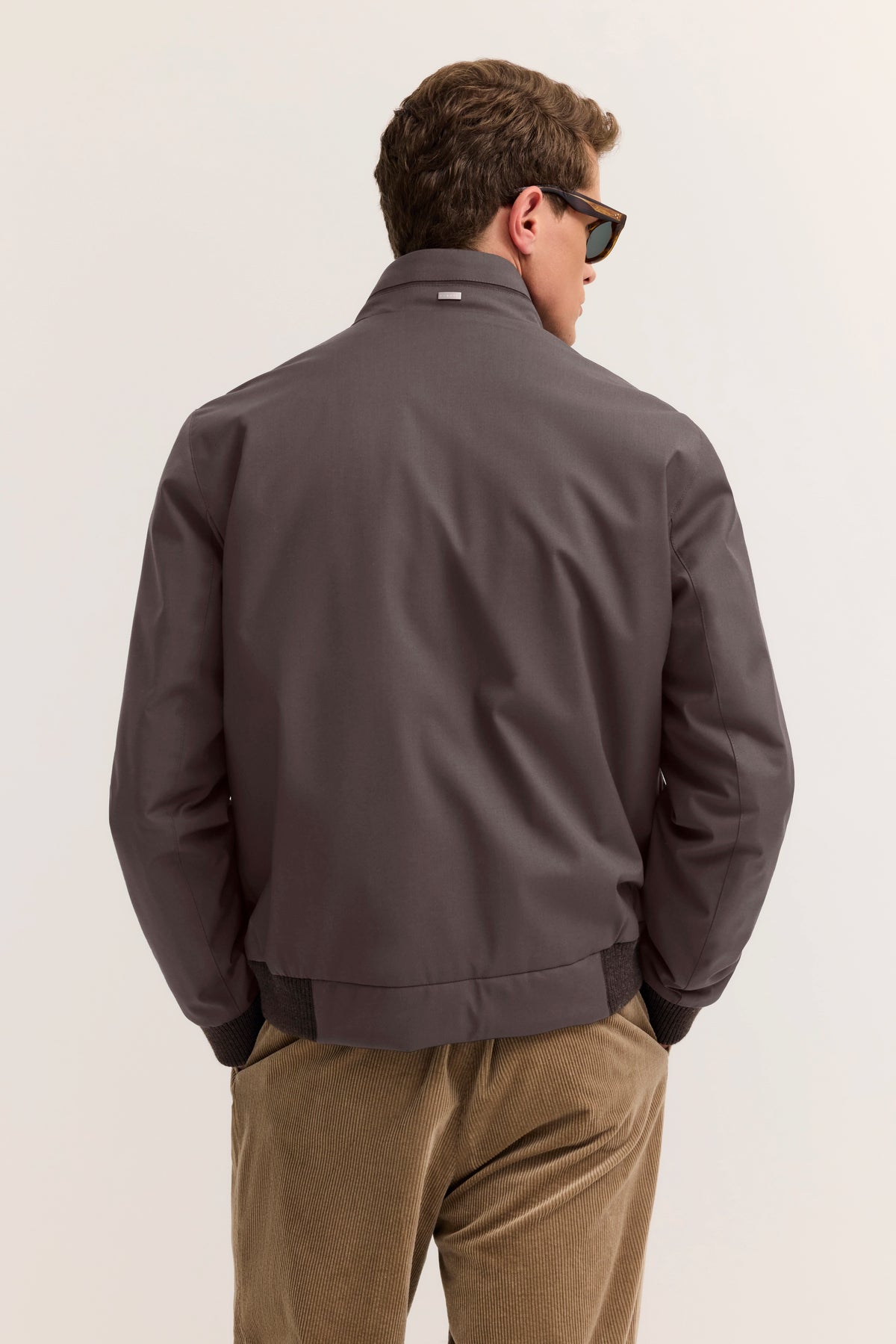 Graue bugatti Jacke Rückansicht, Model trägt braune Cordhose, lässig mit Händen in den Taschen.