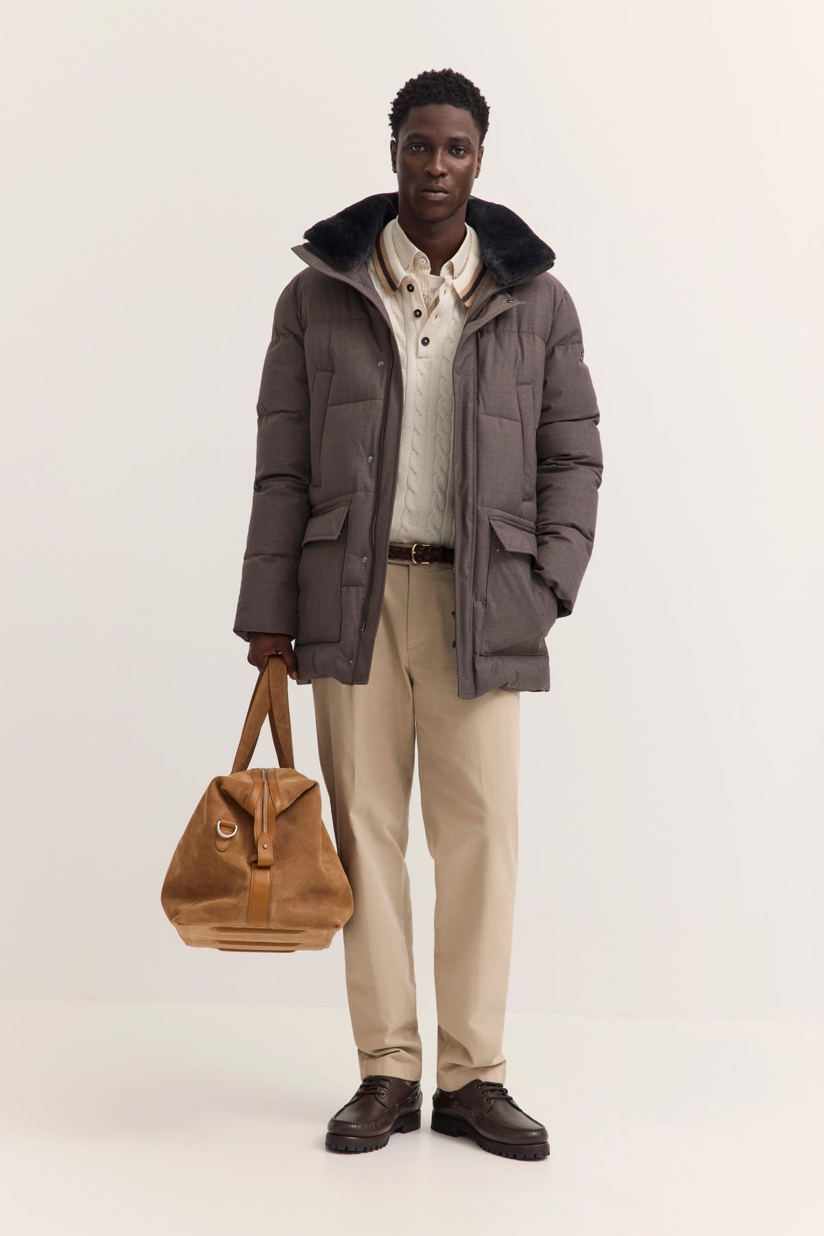 Model in grauer bugatti Daunenjacke, beigem Strickpullover, khakifarbenen Hosen und braunen Schuhen.
