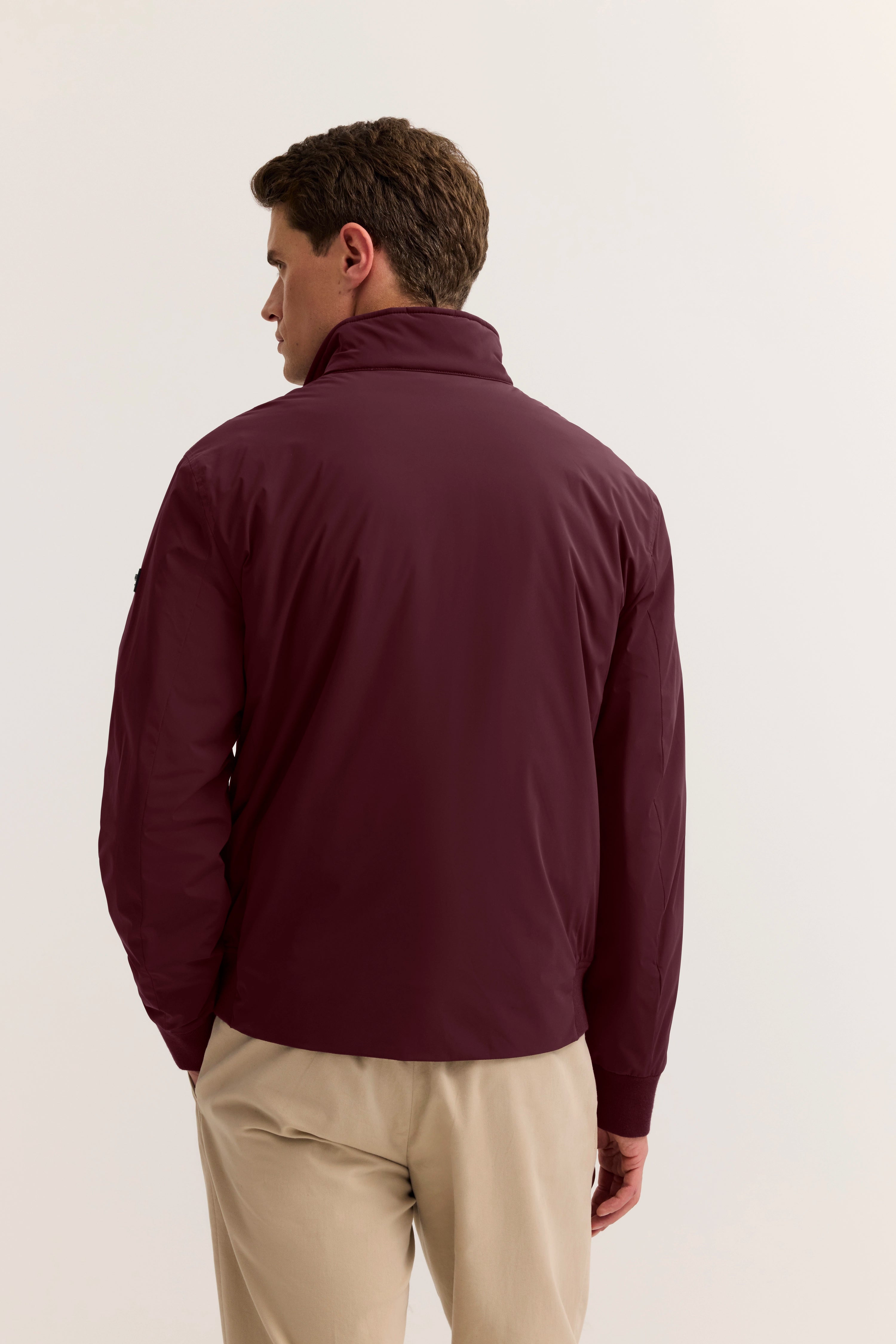 Rückansicht eines Models in bordeauxfarbener bugatti-Jacke und beigen Hosen.