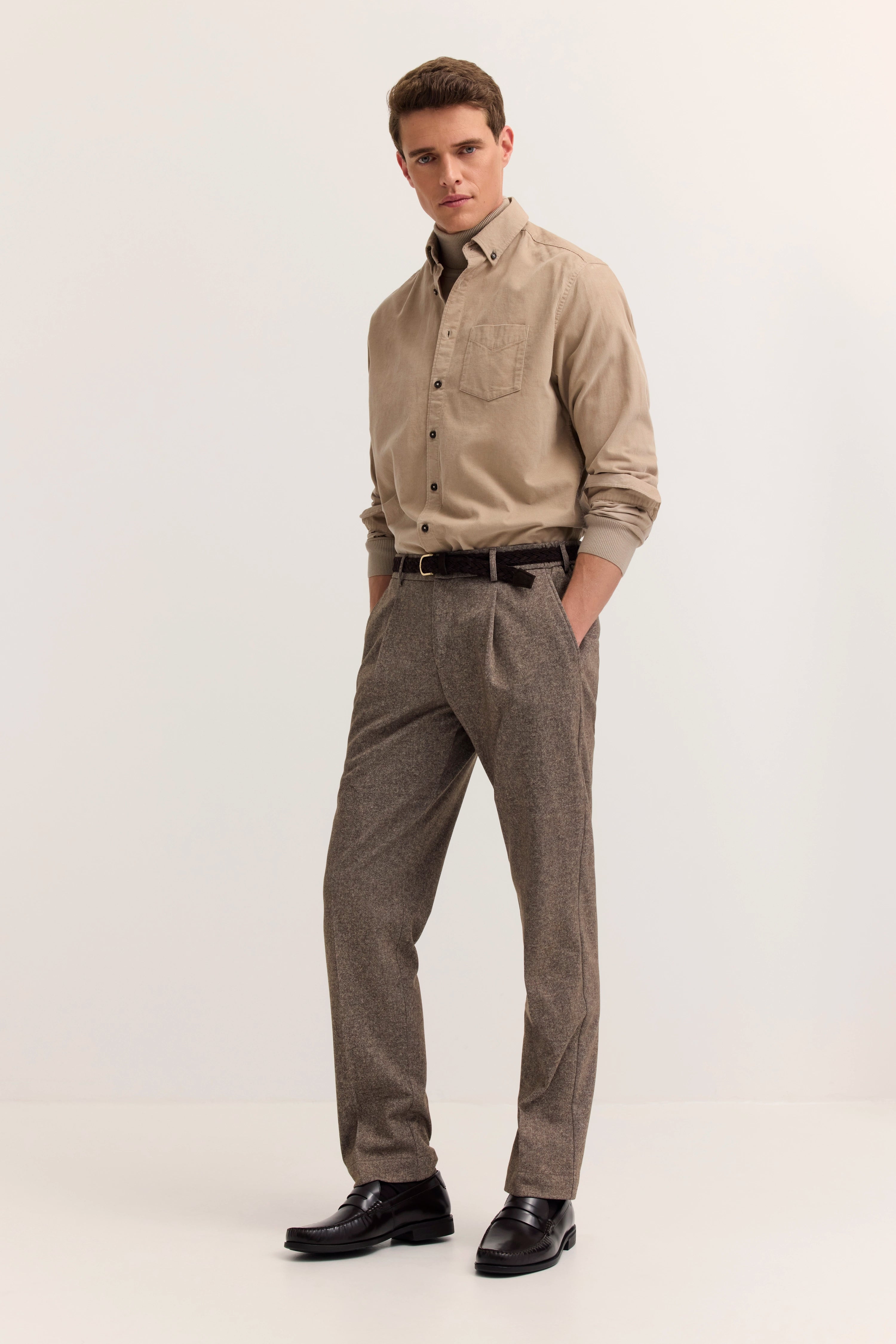Beiges Hemd und graue Hose, Model stehend mit Händen in den Taschen, bugatti Stil.