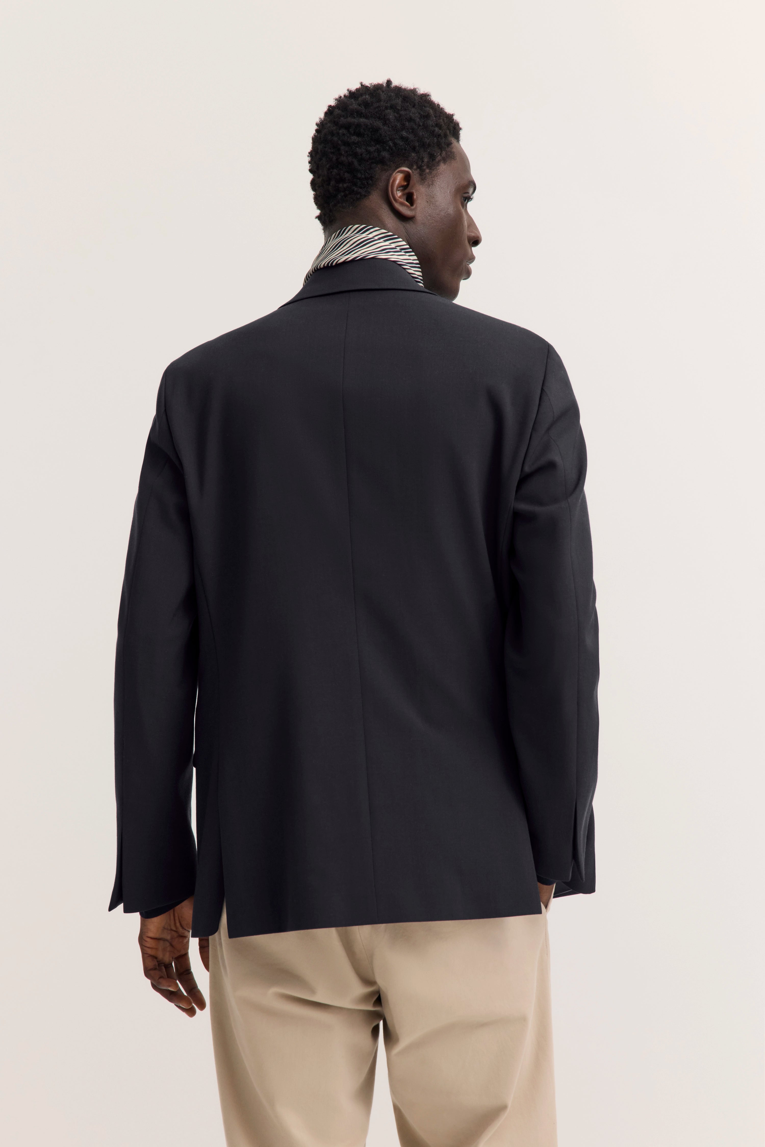 Rückansicht eines Models trägt schwarzen bugatti Blazer und beige Hose, lässig stehend.