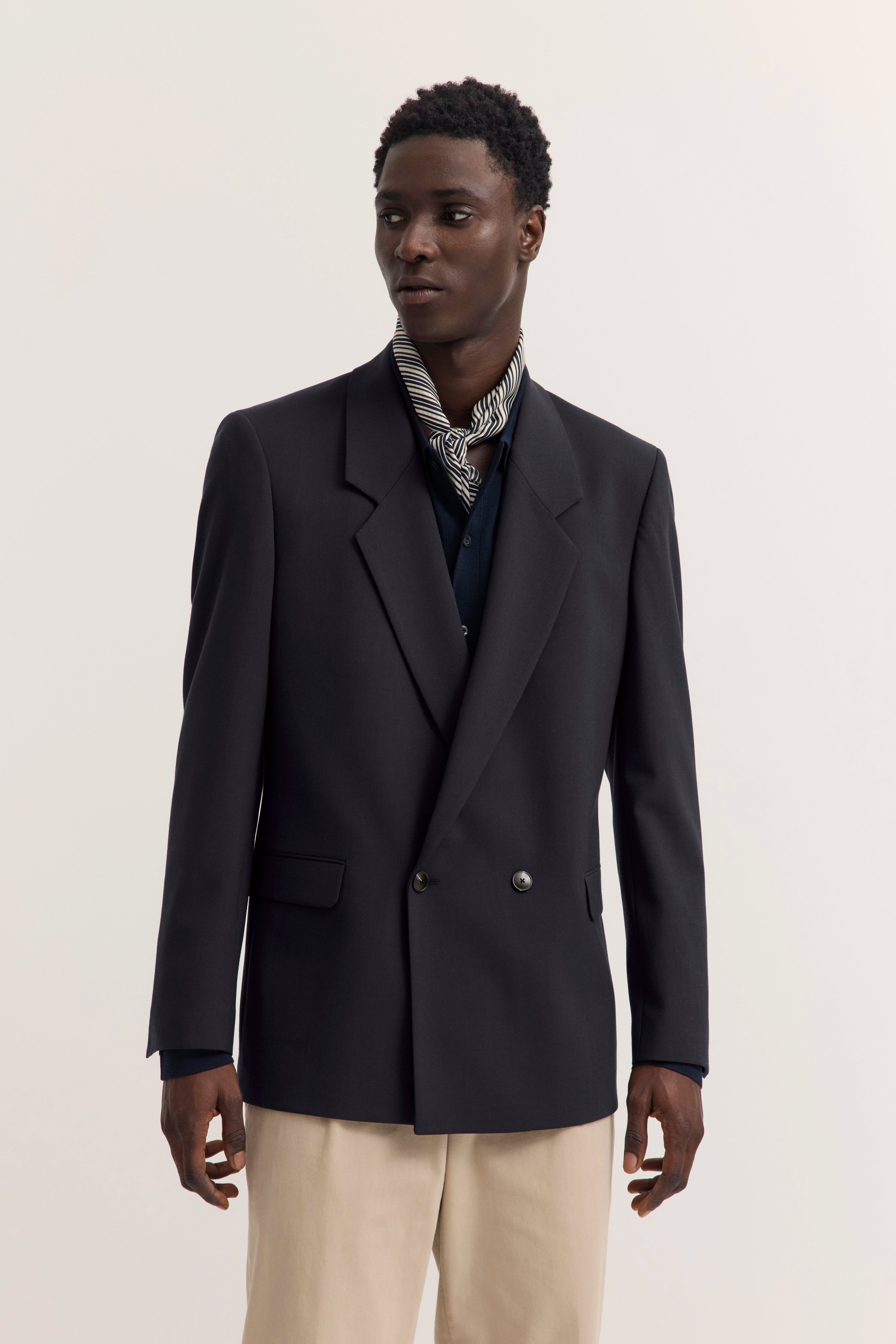 Model in bugatti Doppelreiher-Blazer, dunkel, mit gestreiftem Hemd und beigen Hosen, elegantes Posing.