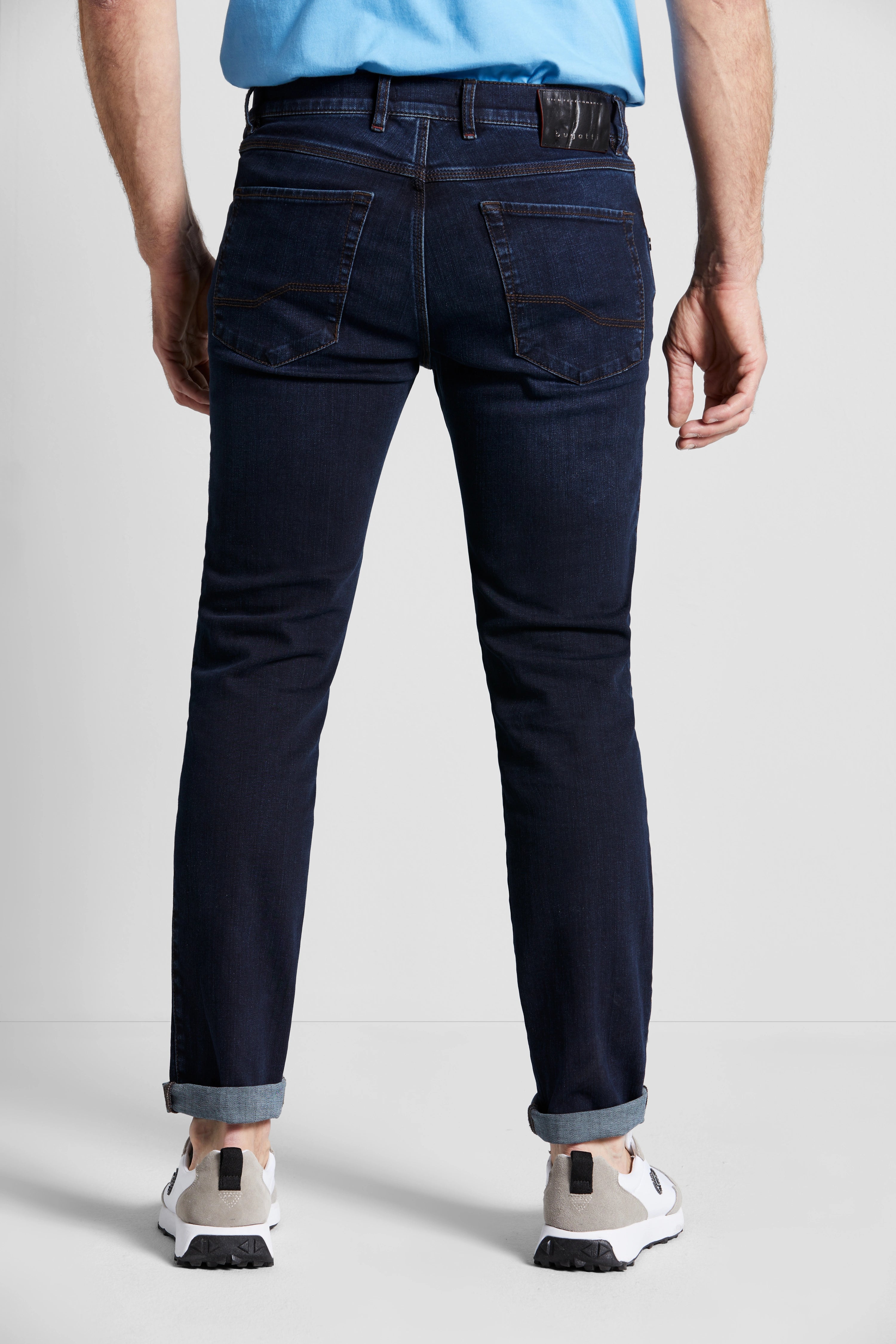 Dunkelblaue bugatti Jeans, legeres Modelbild, Rückenansicht, kombiniert mit hellblauem Oberteil.