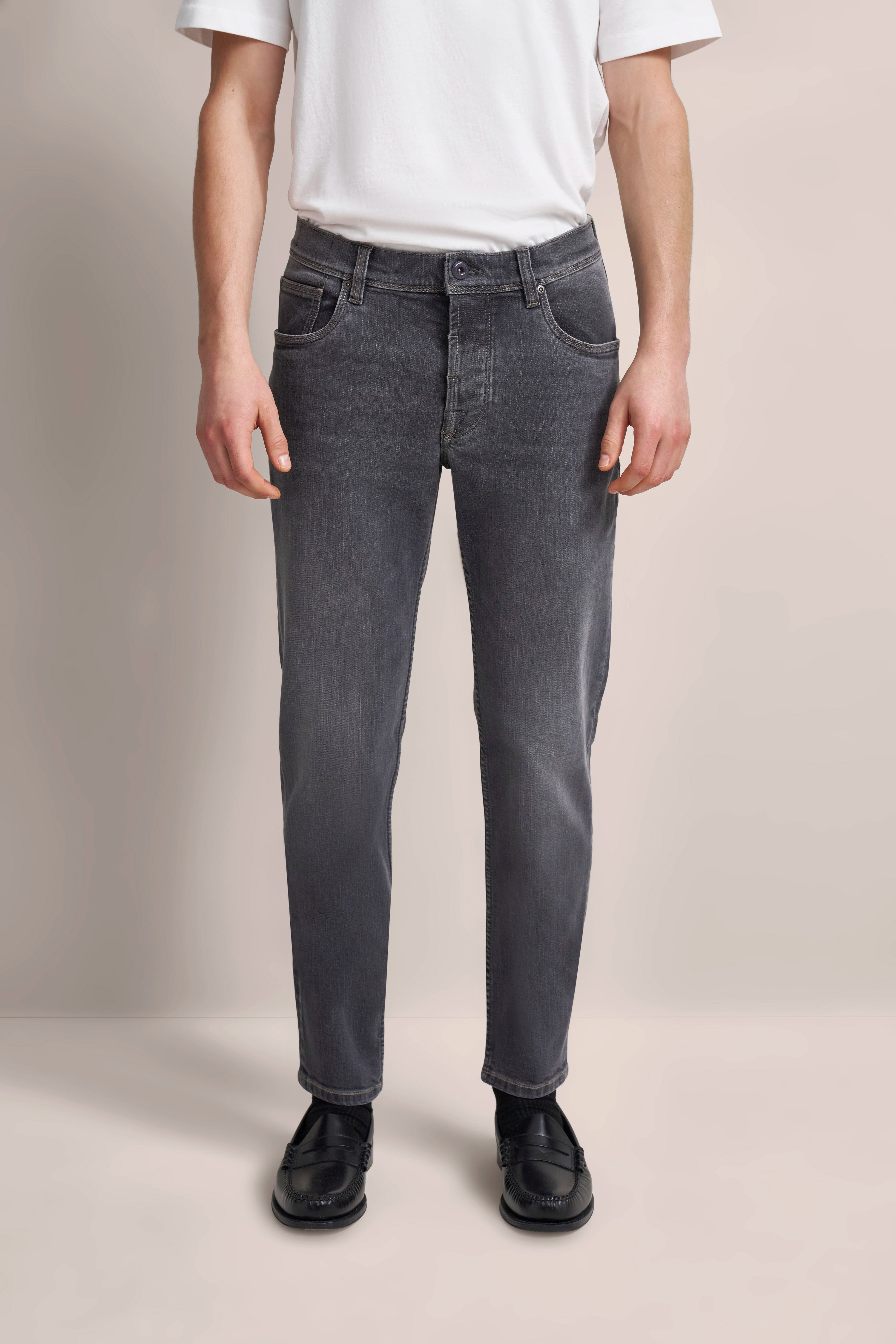 Graue Jeans und weißes Shirt, legeres Modelbild, entspannte Haltung.