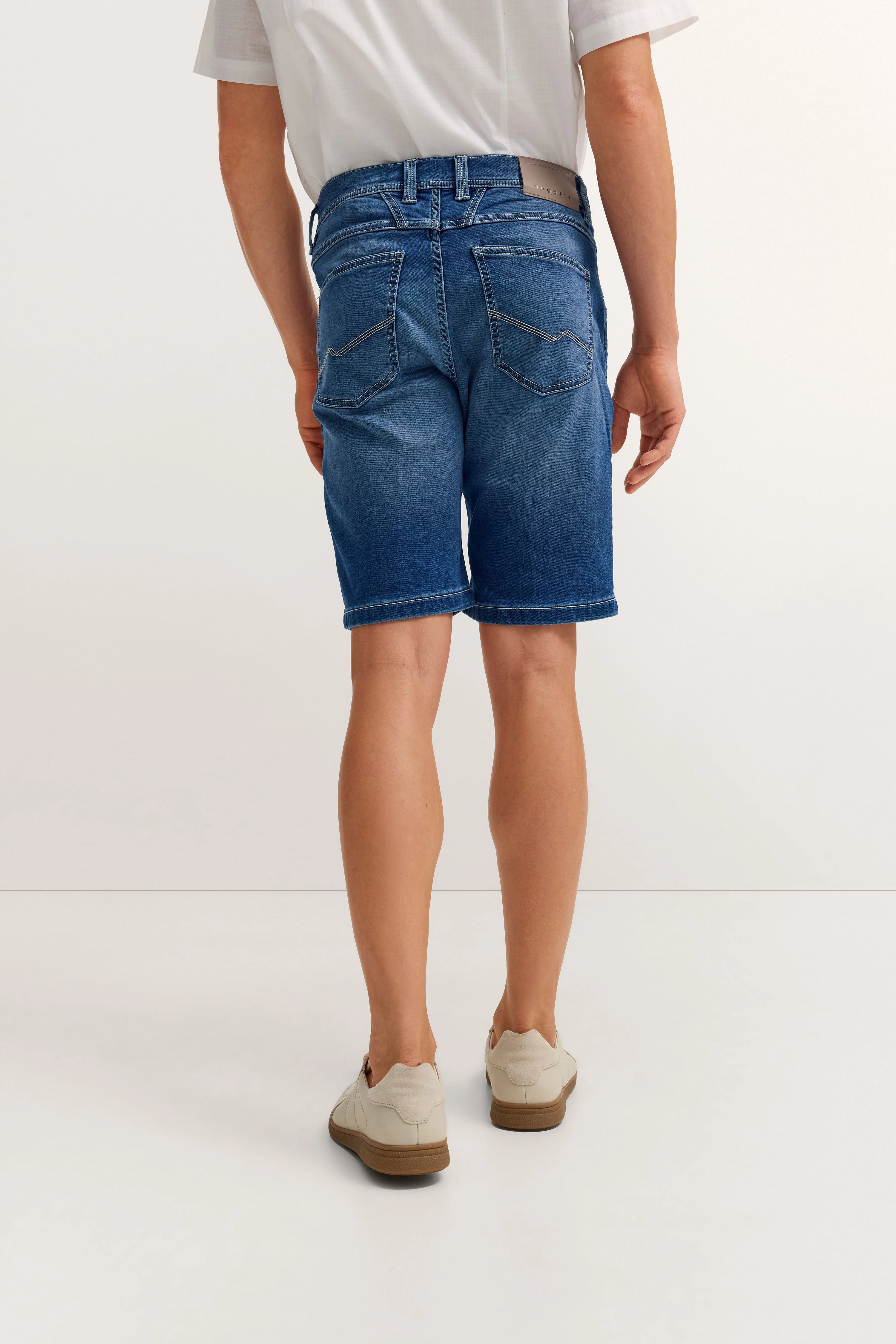 bugatti Jeansshorts in Blau, legeres Modelbild von hinten, weißes Hemd, beige Sneaker.