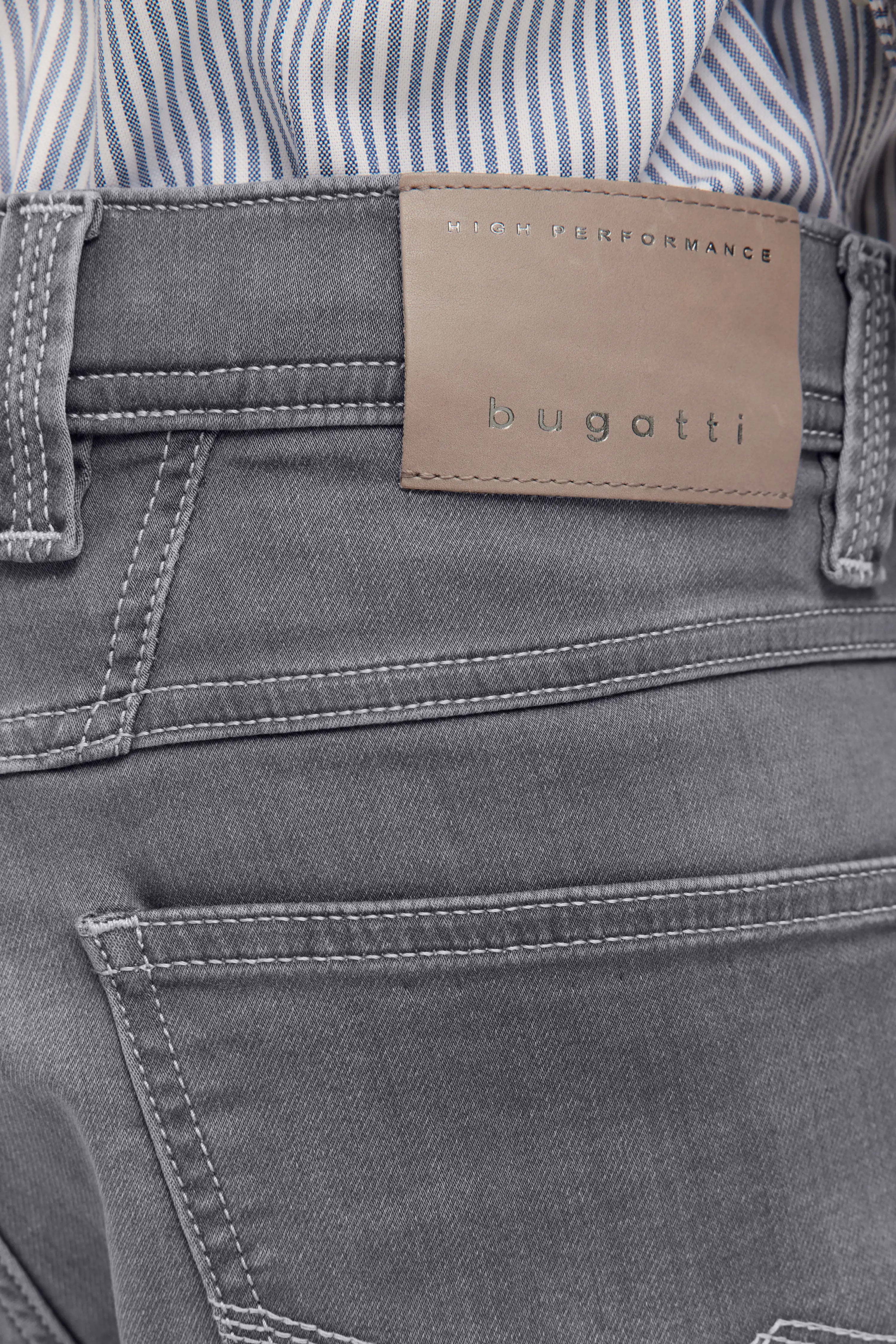 Graue bugatti-Jeans mit Label, kombiniert mit gestreiftem Hemd. Legeres Büstenbild.