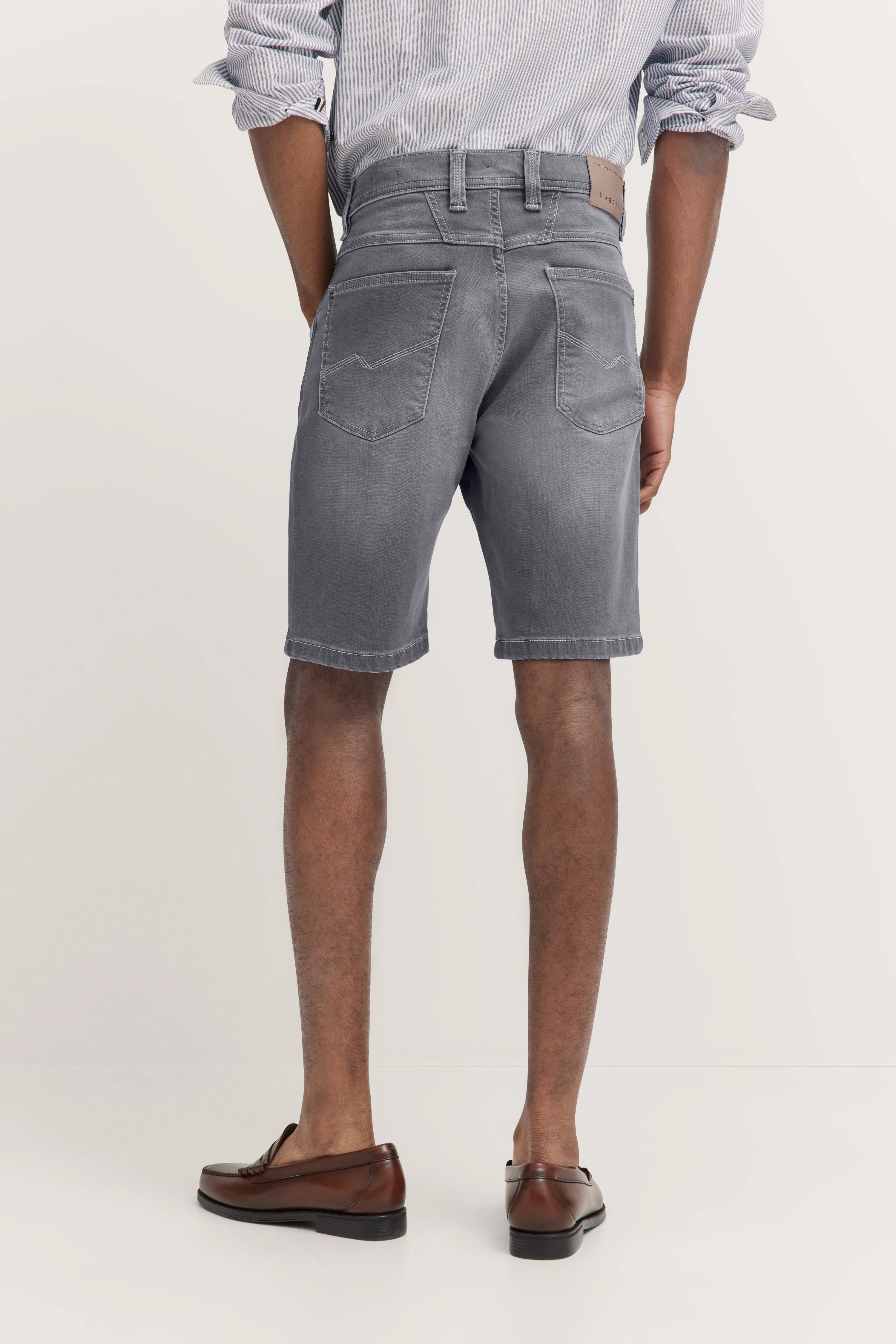 bugatti Model in grauen Shorts, gestreiftem Hemd, braunen Schuhen, entspannte Pose, Rückansicht.