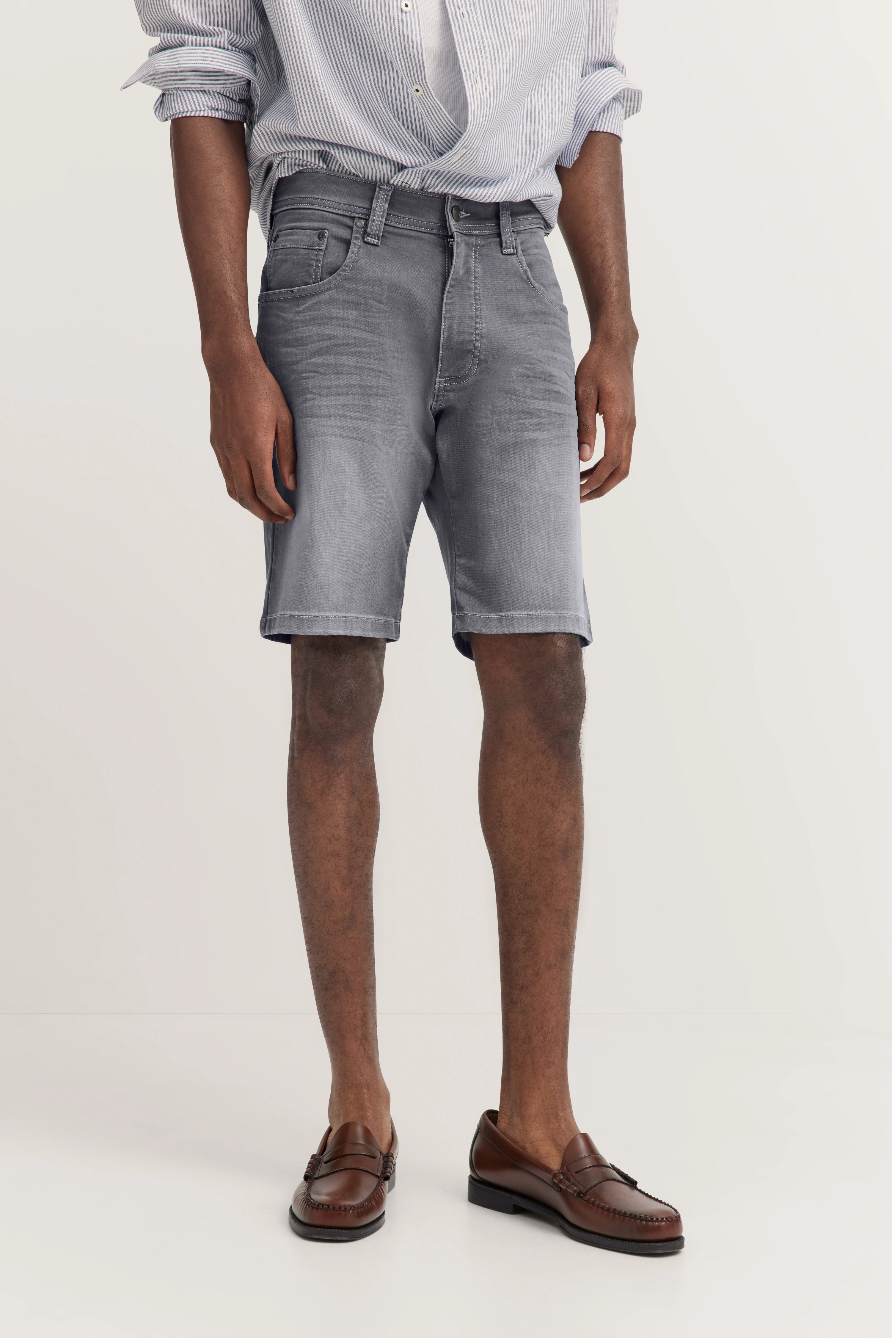 Graues Kurzarmoutfit mit gestreiftem Hemd und braunen Loafern, legeres Modelbild mit entspanntem Posing.