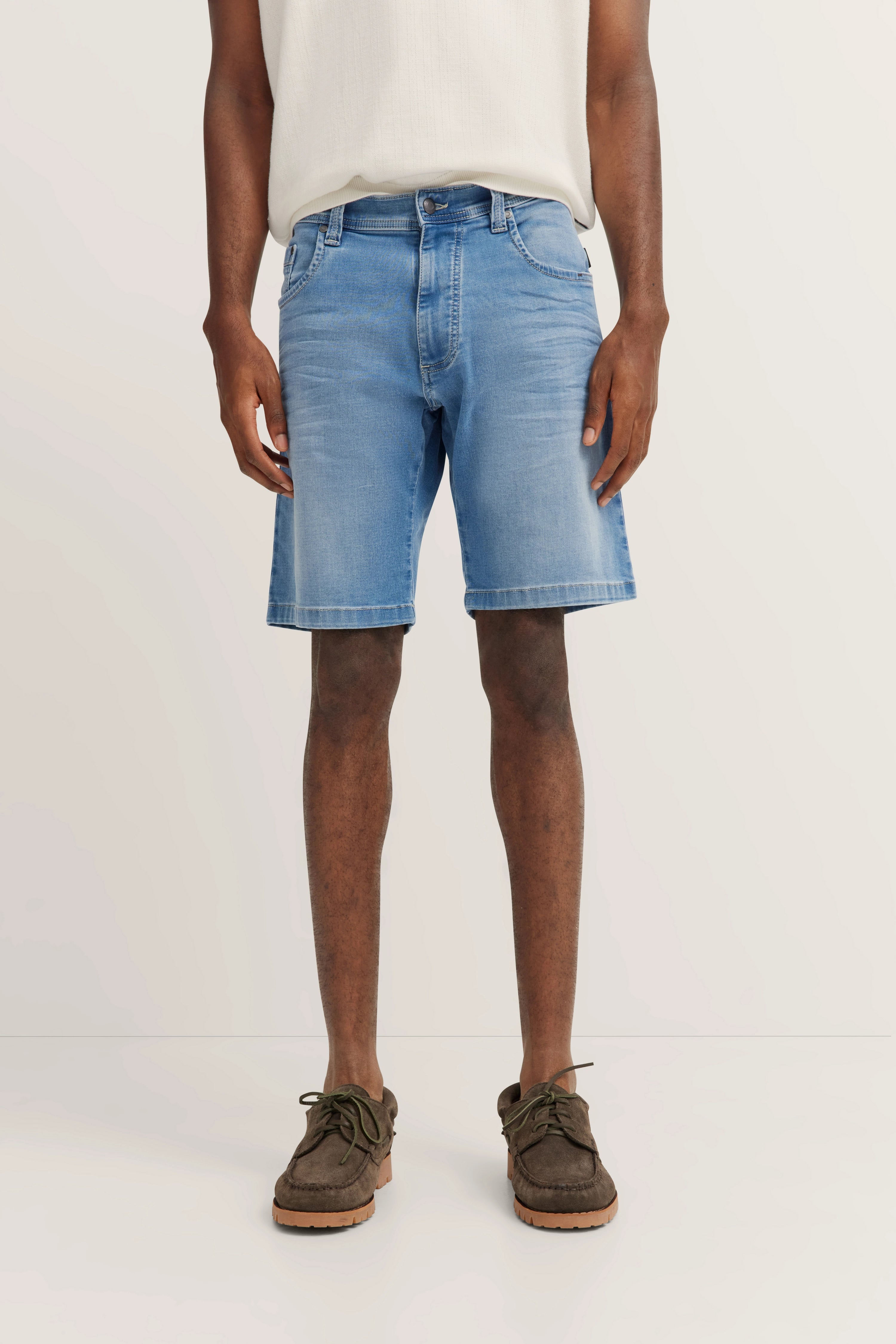 bugatti Modelbild, helles Shirt, blaue Jeansshorts, entspannte Haltung, grüne Mokassins.