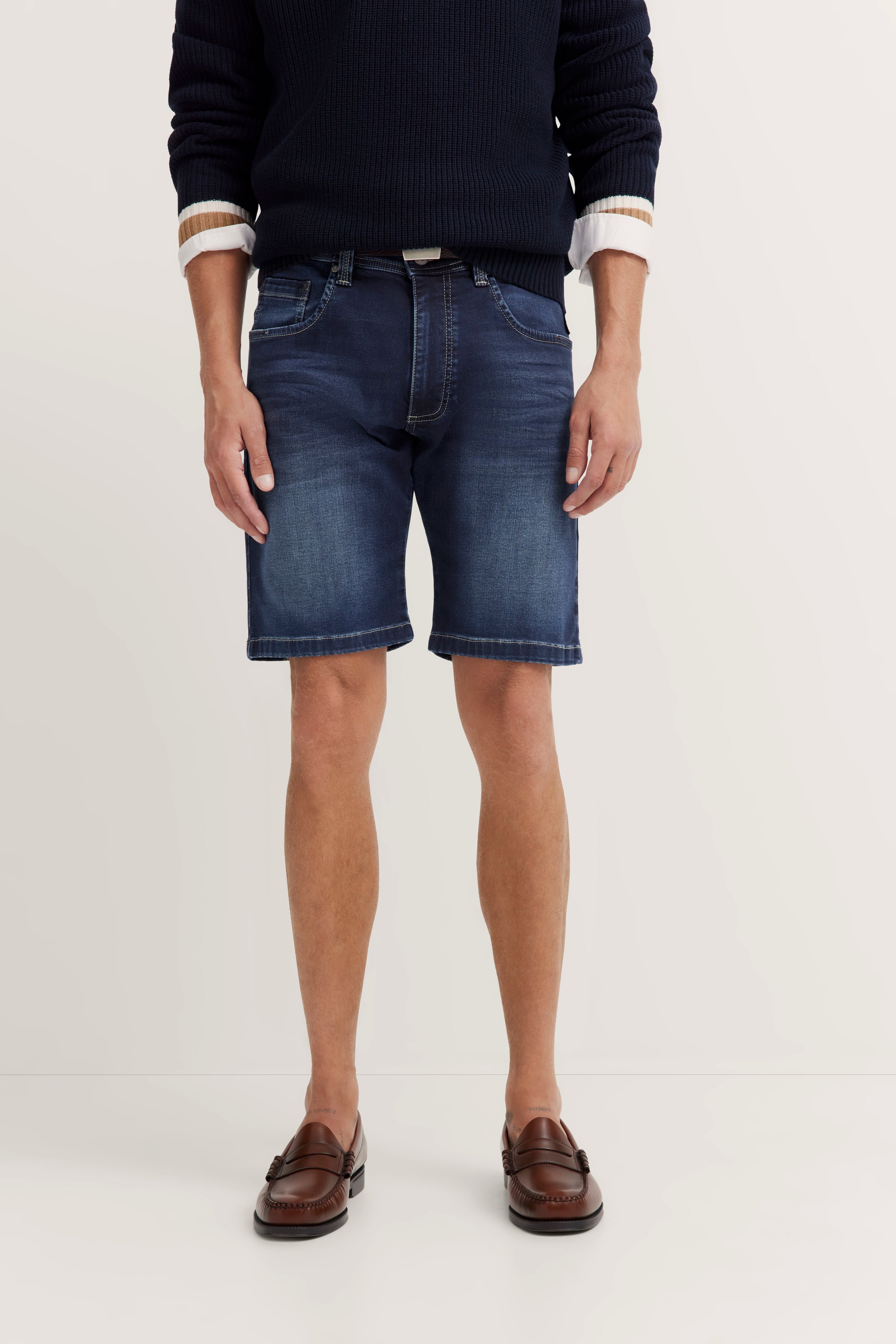 bugatti Modelbild: Dunkelblauer Pullover, blaue Jeansshorts, braune Loafers. Lässig stehend, entspannte Pose.