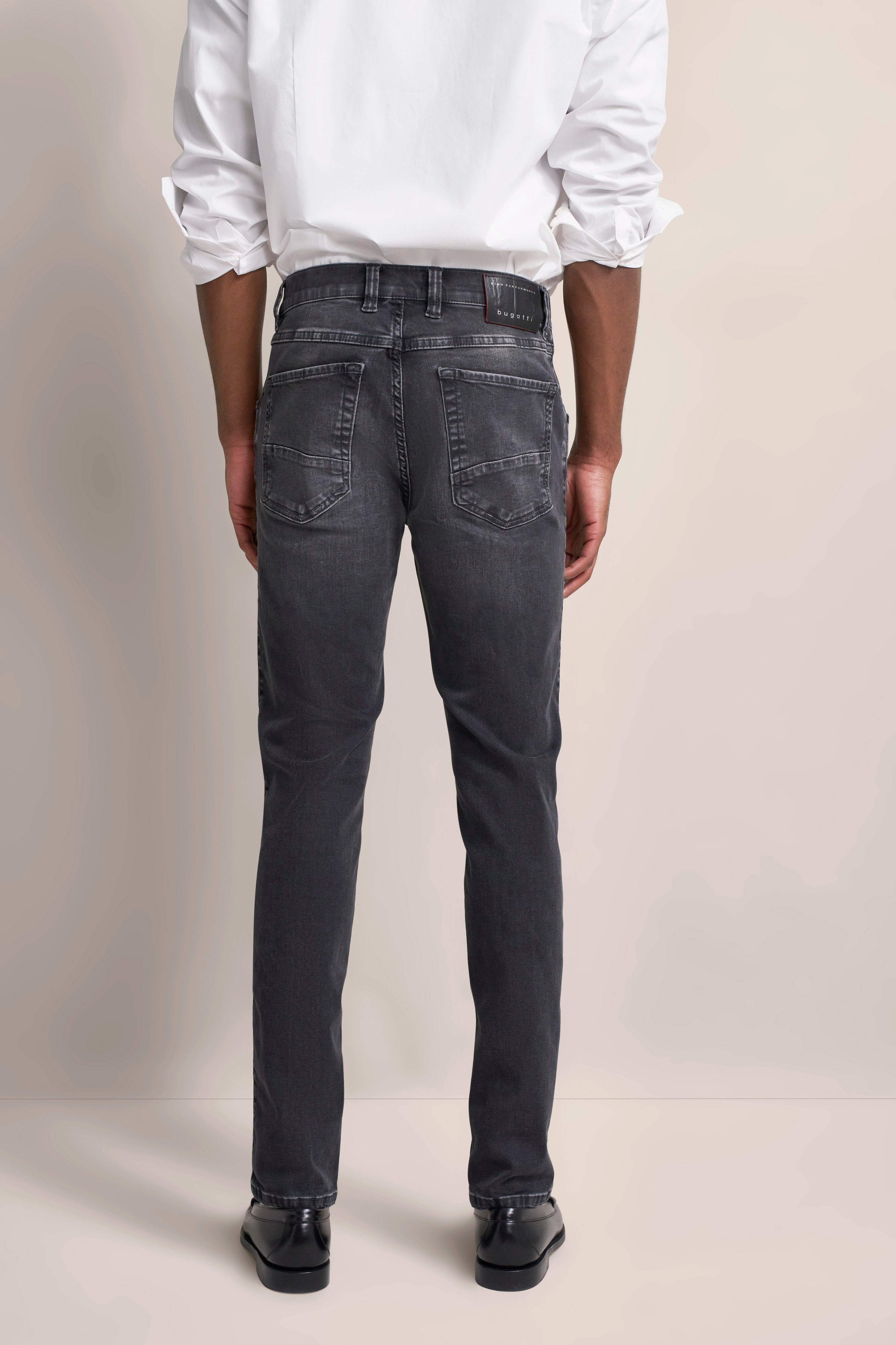 Modelbild: Weißes Hemd, graue Jeans von bugatti. Rückenansicht, lässige Pose.