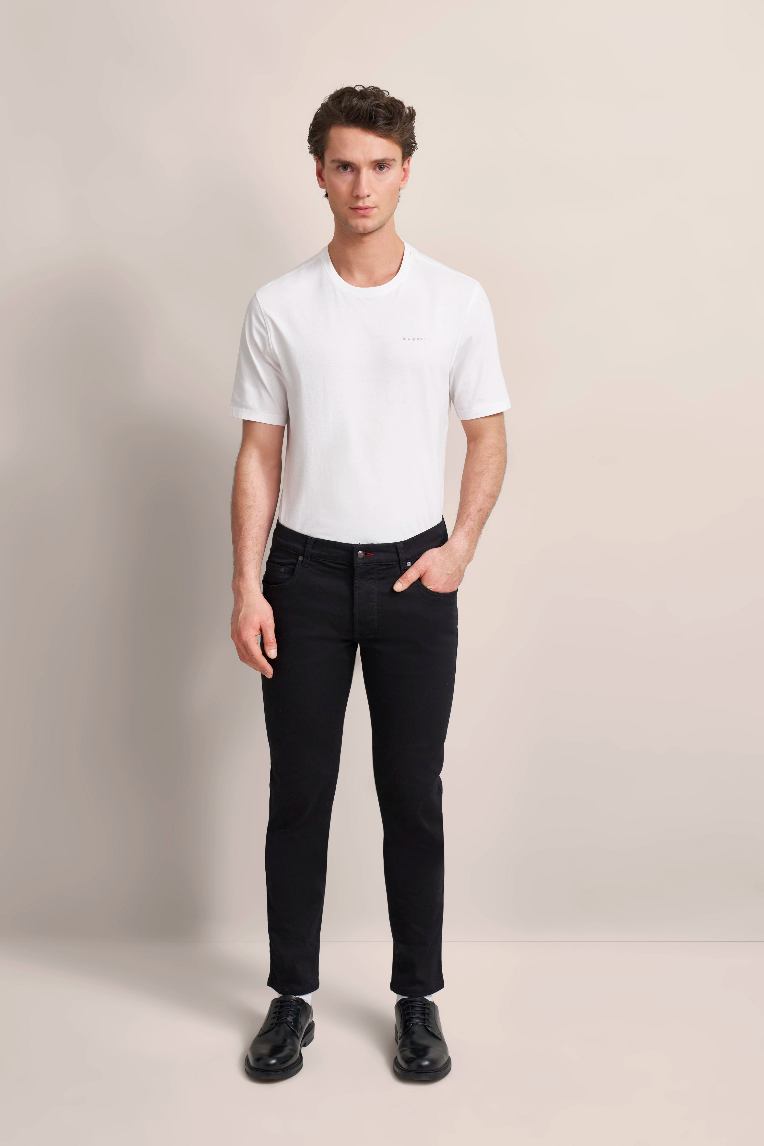 Model in weißem bugatti T-Shirt und schwarzer Jeans, entspannt stehend, elegantes Outfit.