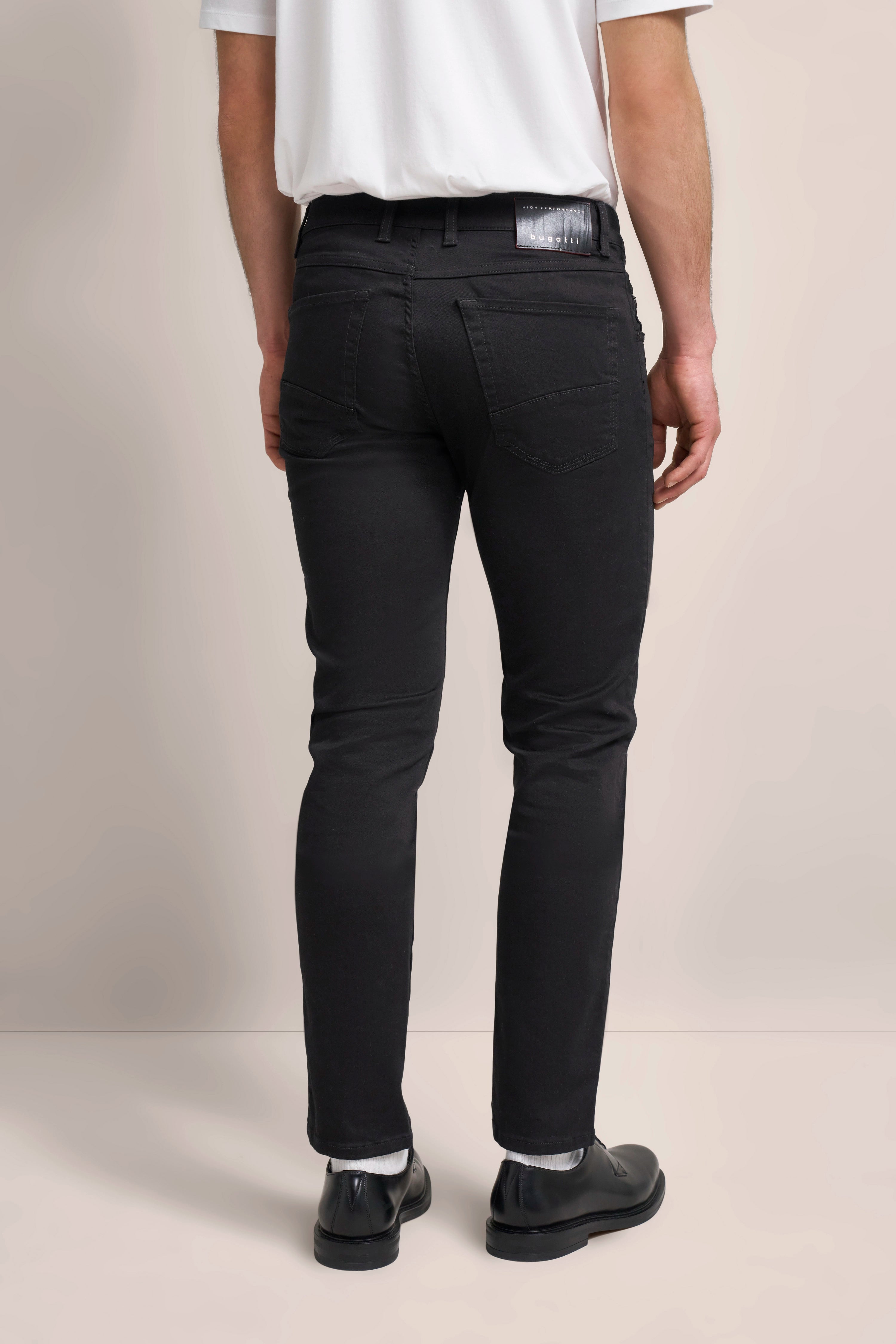 Schwarze bugatti Hose an Model, von hinten, mit weißem Shirt und schwarzen Schuhen.