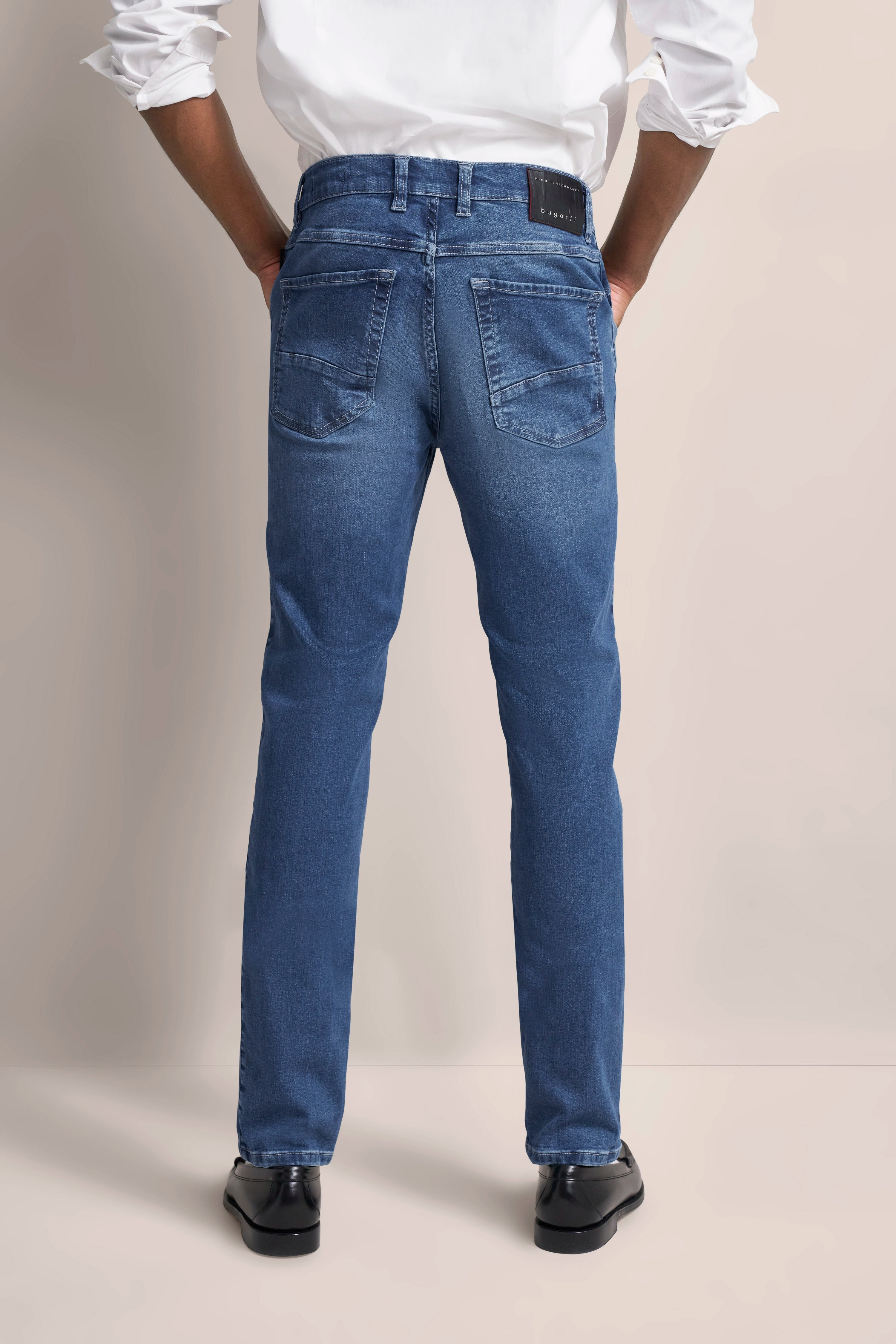 Model in blauer bugatti-Jeans und weißem Hemd von hinten, leger stehend.