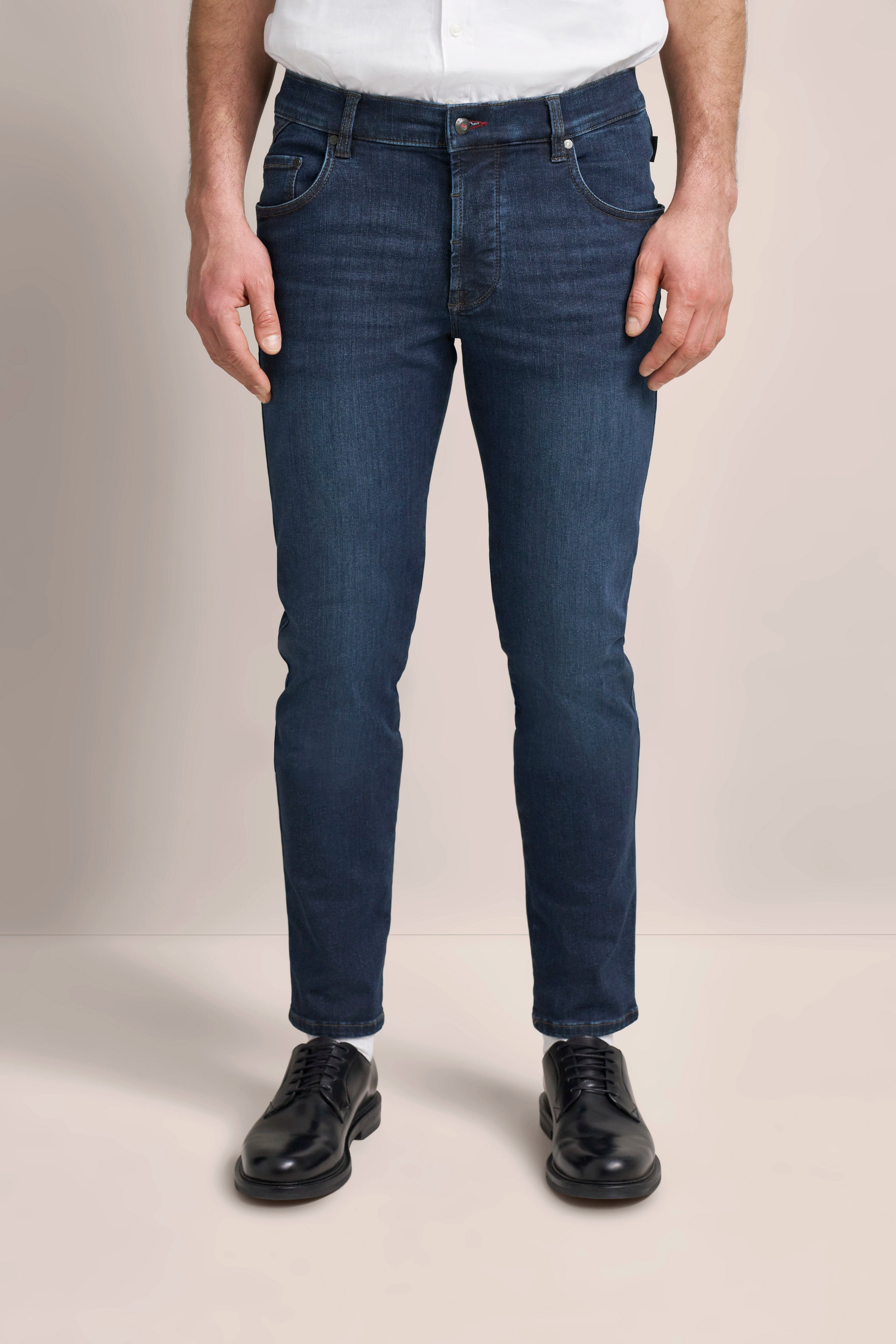 Dunkelblaue Jeans, weißes Hemd, schwarze Schuhe. Modelbild stehend, lässige Pose.
