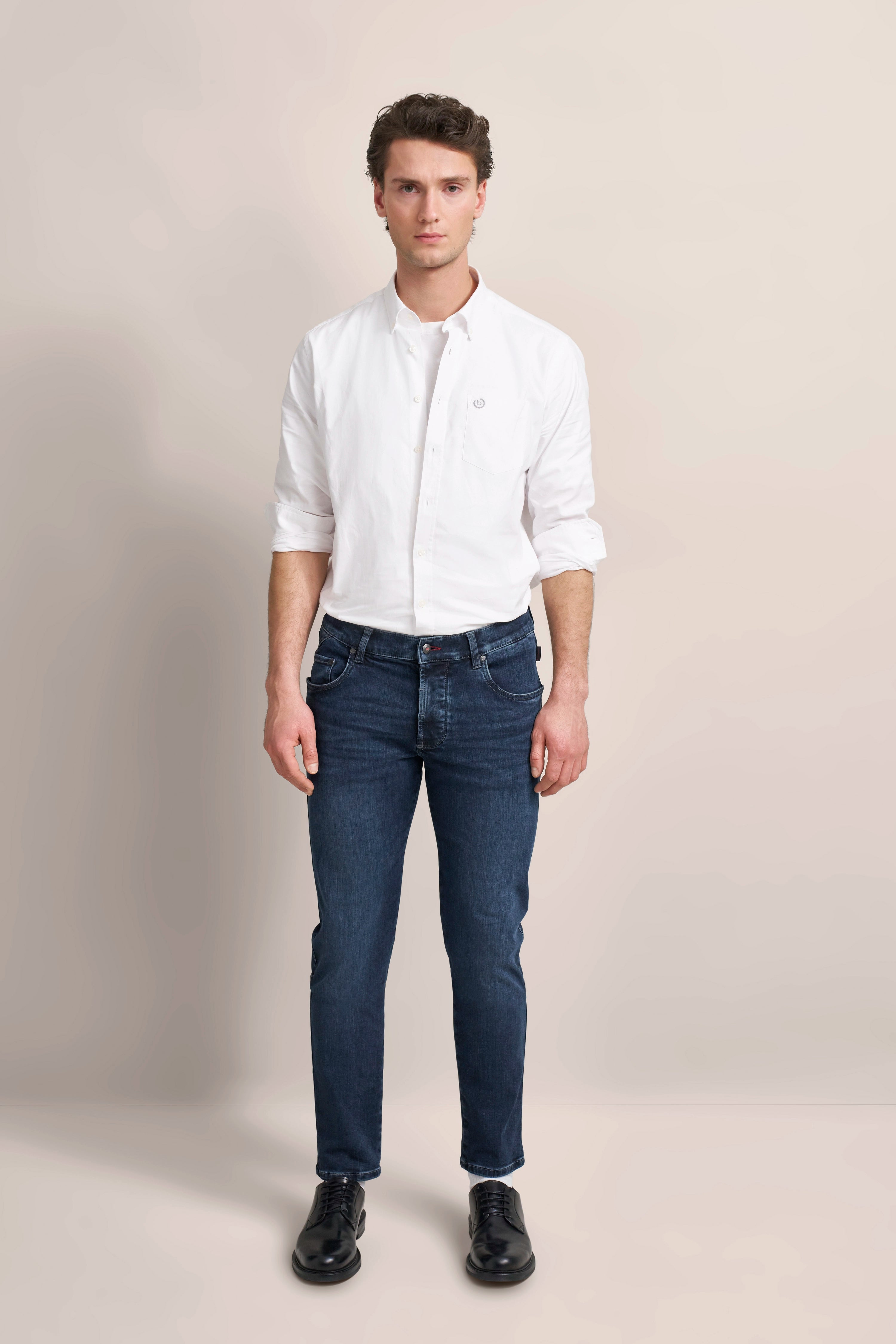 bugatti Model in weißem Hemd, blauen Jeans, schwarze Schuhe, entspannte Pose, urbaner Stil.