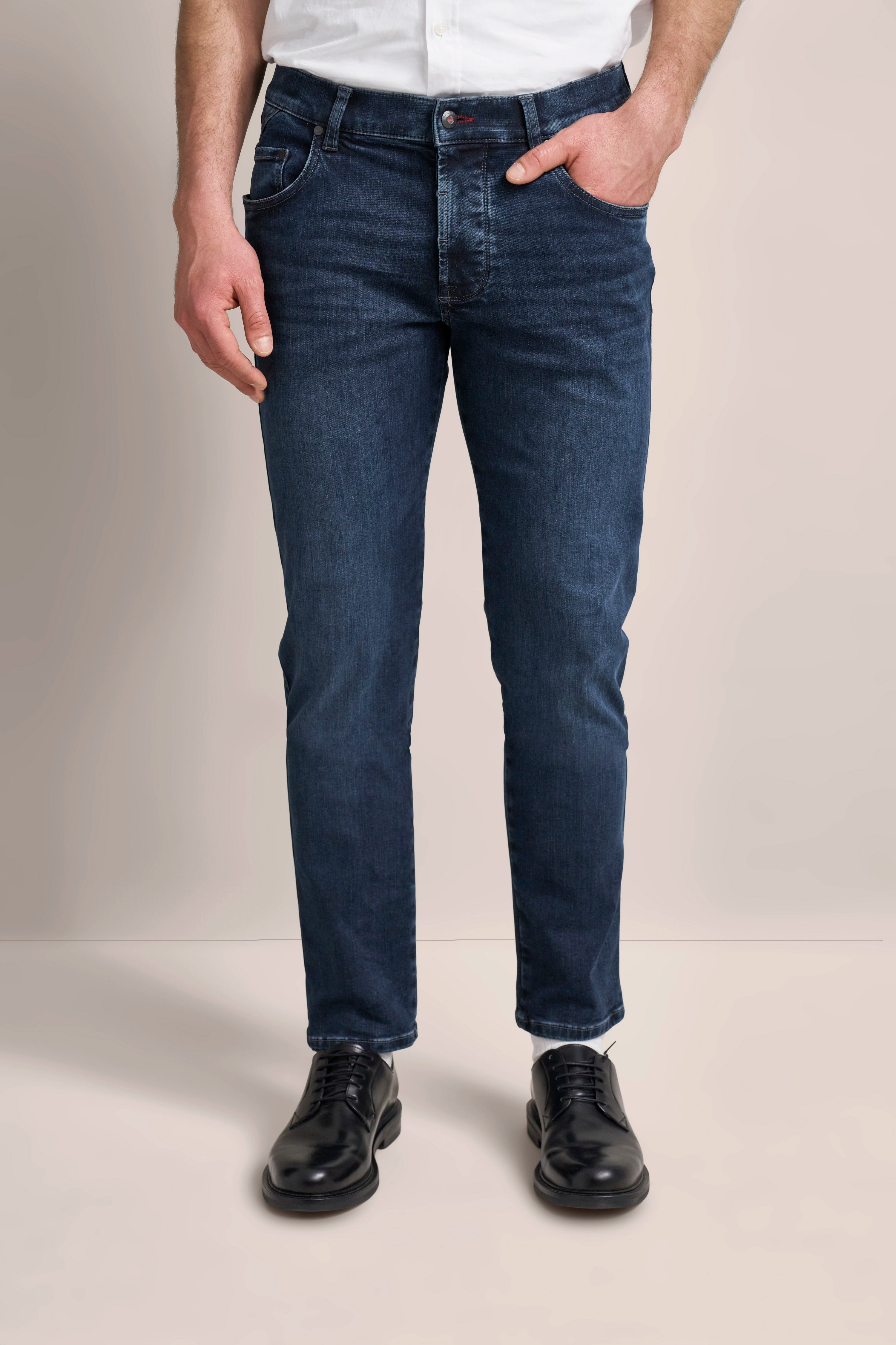 Dunkelblaue Jeans, weißes Hemd, schwarze Schuhe, legeres Modelbild, Hände in Hosentaschen.