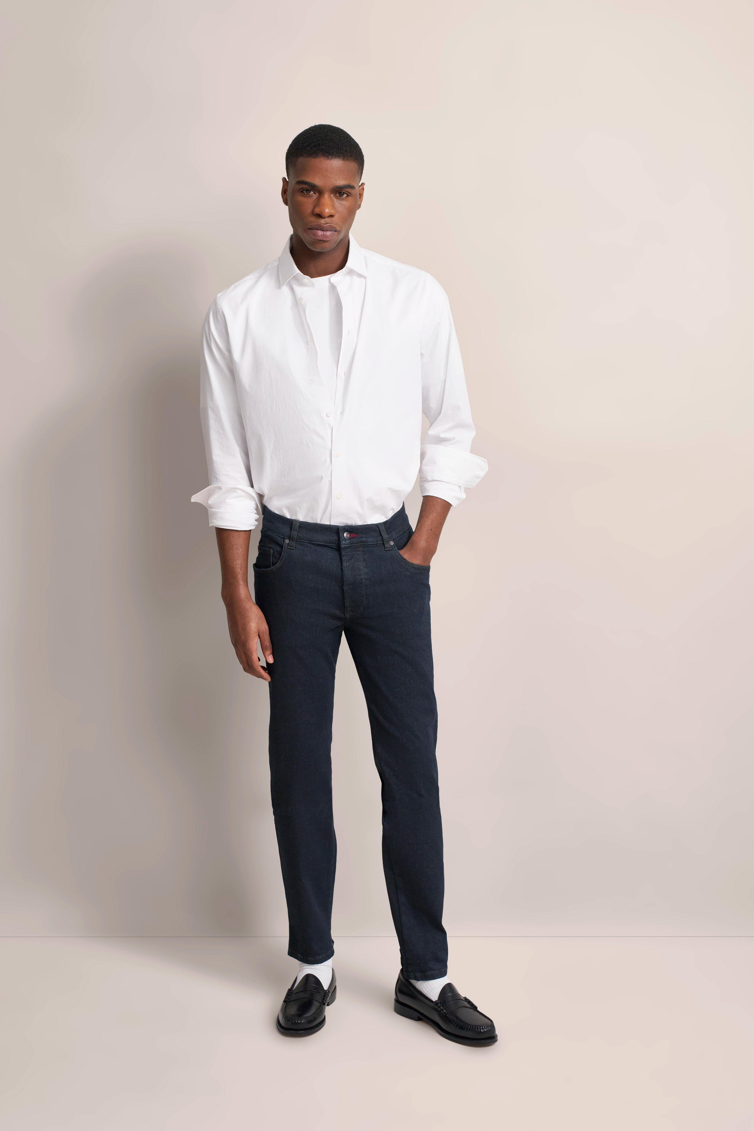 Model in weißem Hemd und dunkelblauer Jeans von bugatti, locker stehend.