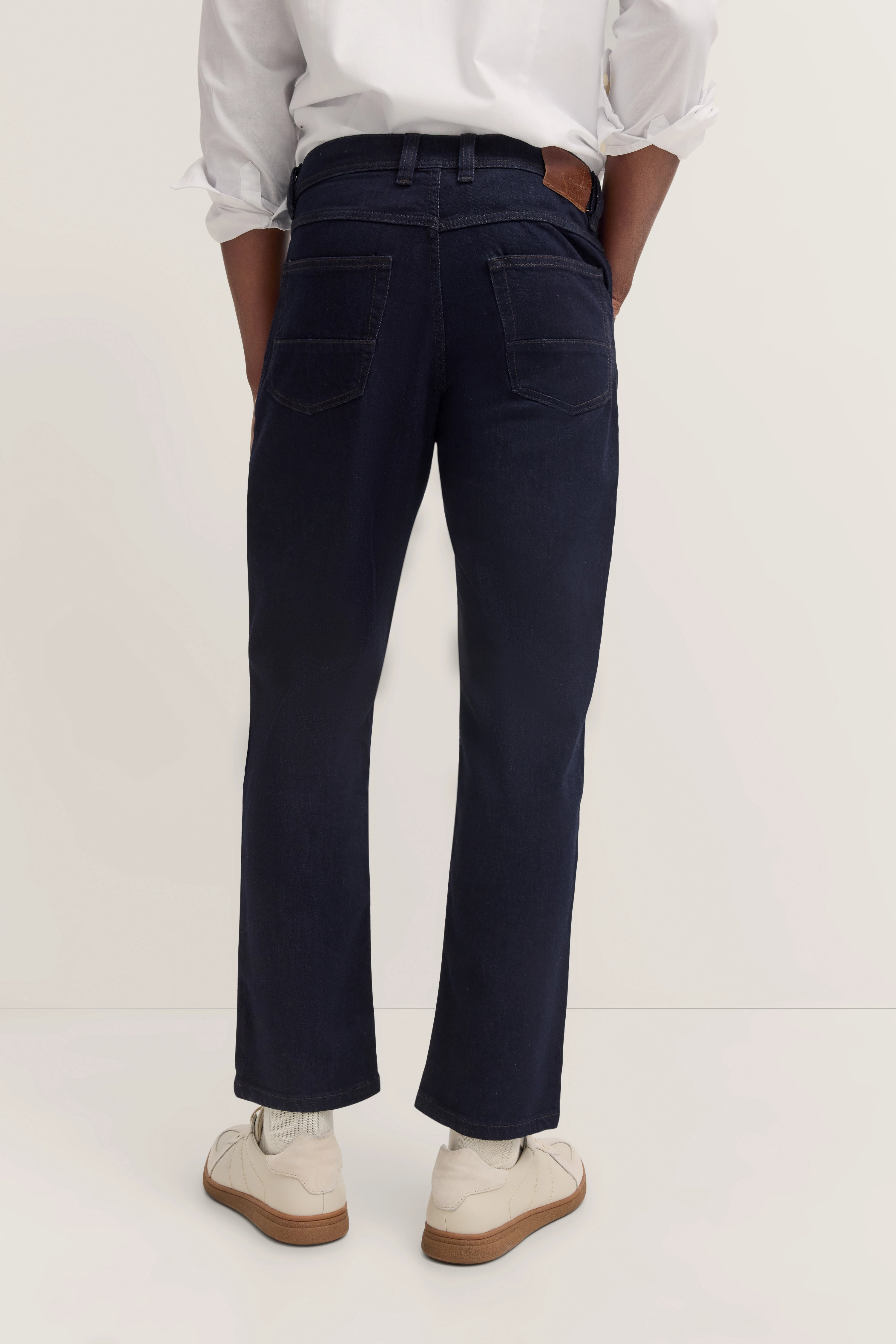 Legerbild: Dunkelblaue Jeans von bugatti mit weißem Hemd und cremefarbenen Sneakern.