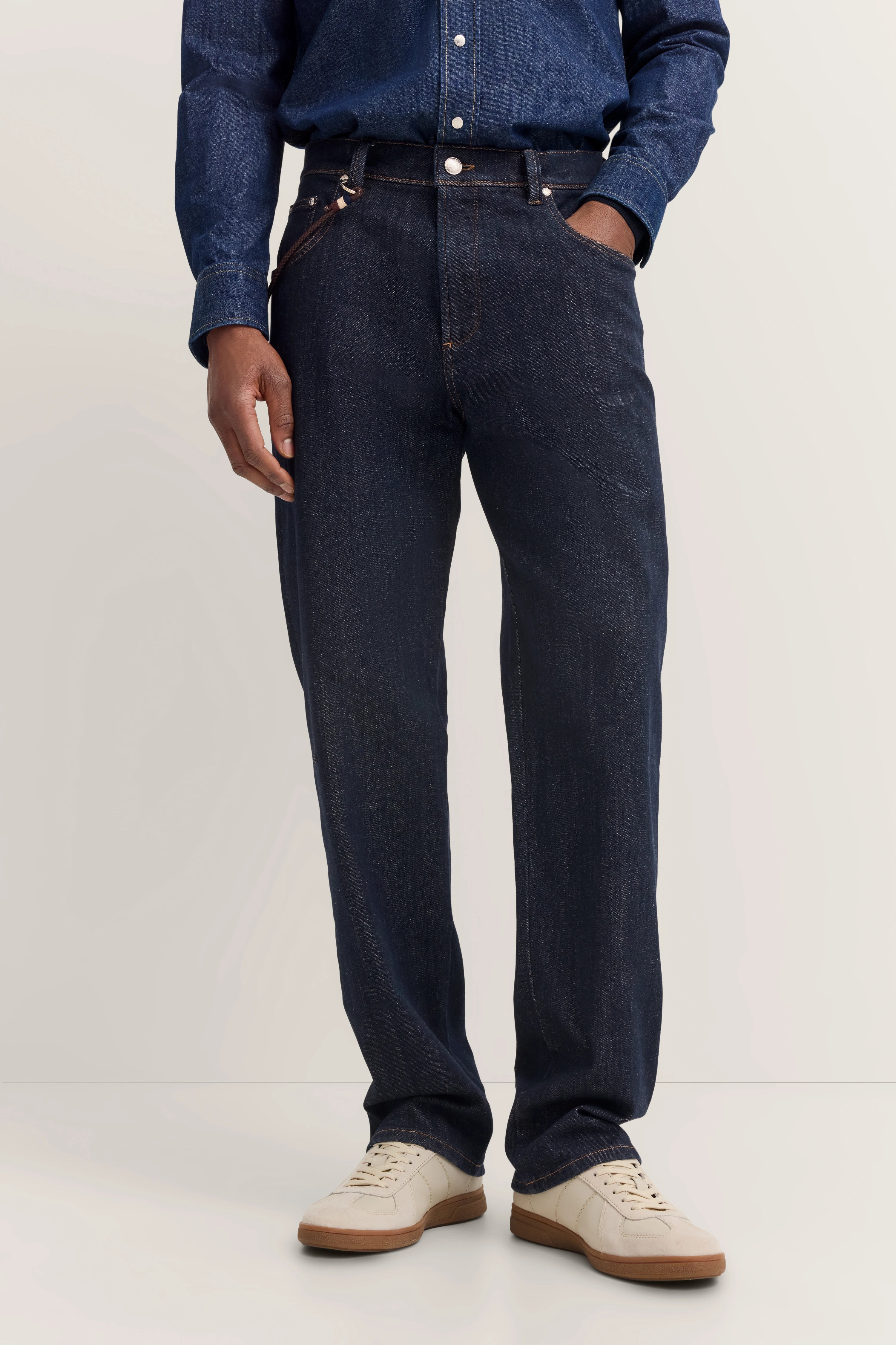 Jeans in Dunkelblau mit Hemd und Sneakern, legeres Modelbild, Hände in Hosentaschen.
