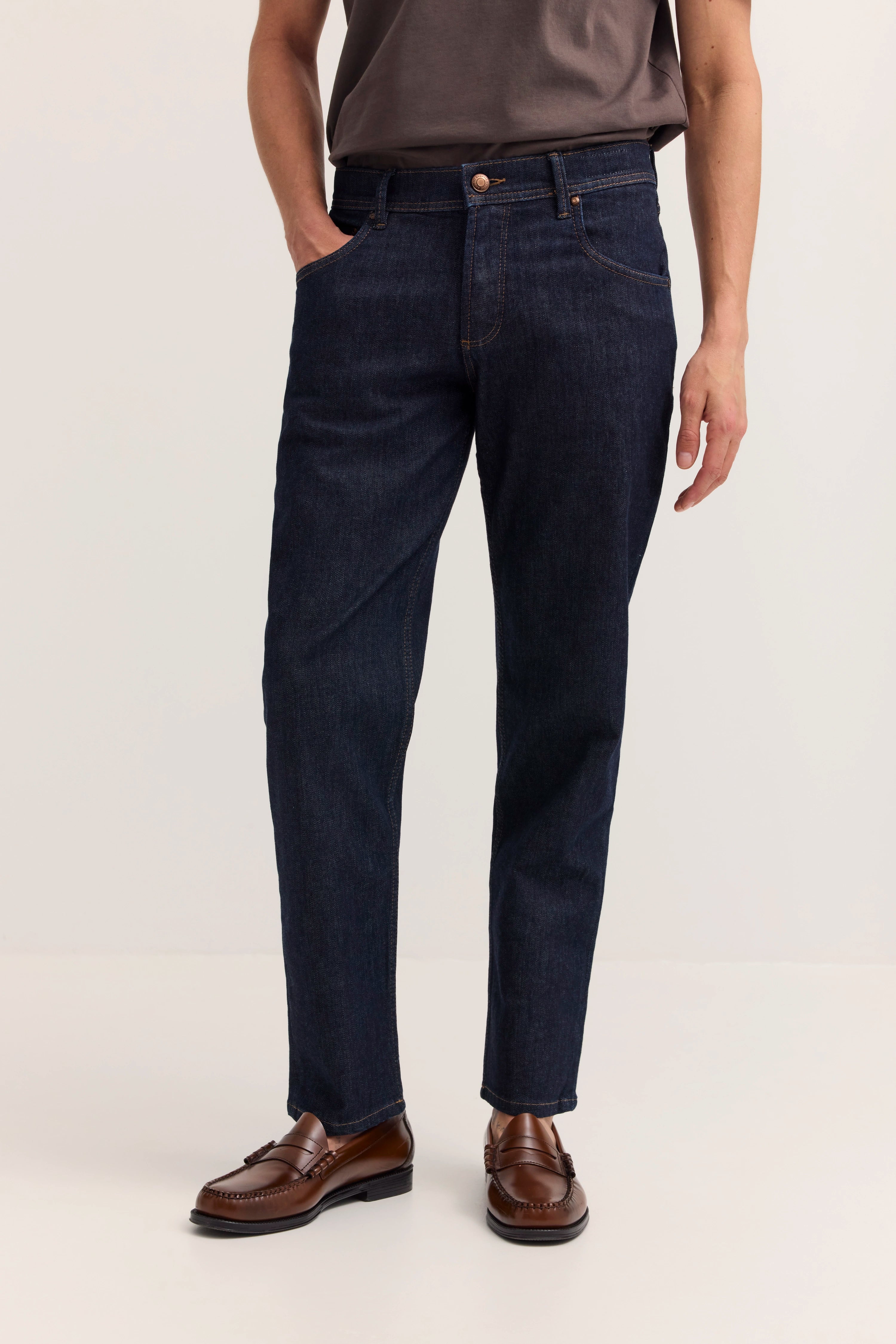 Dunkelblaue Jeans mit braunen Loafern, legeres Modelbild, stehende Pose.