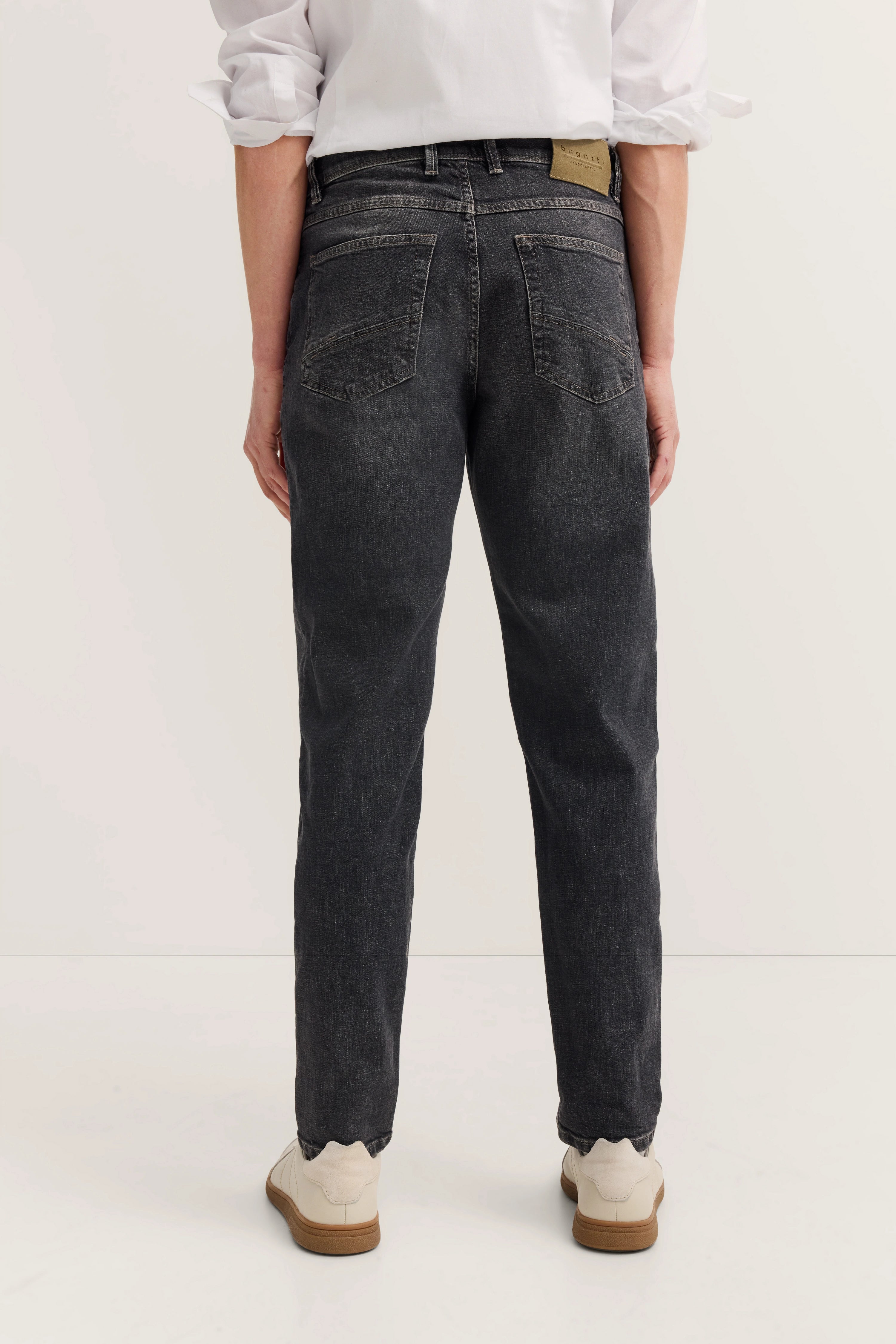 bugatti Jeans in Dunkelgrau, legeres Modelbild, Rückansicht, lässige Passform, weiße Sneakers.