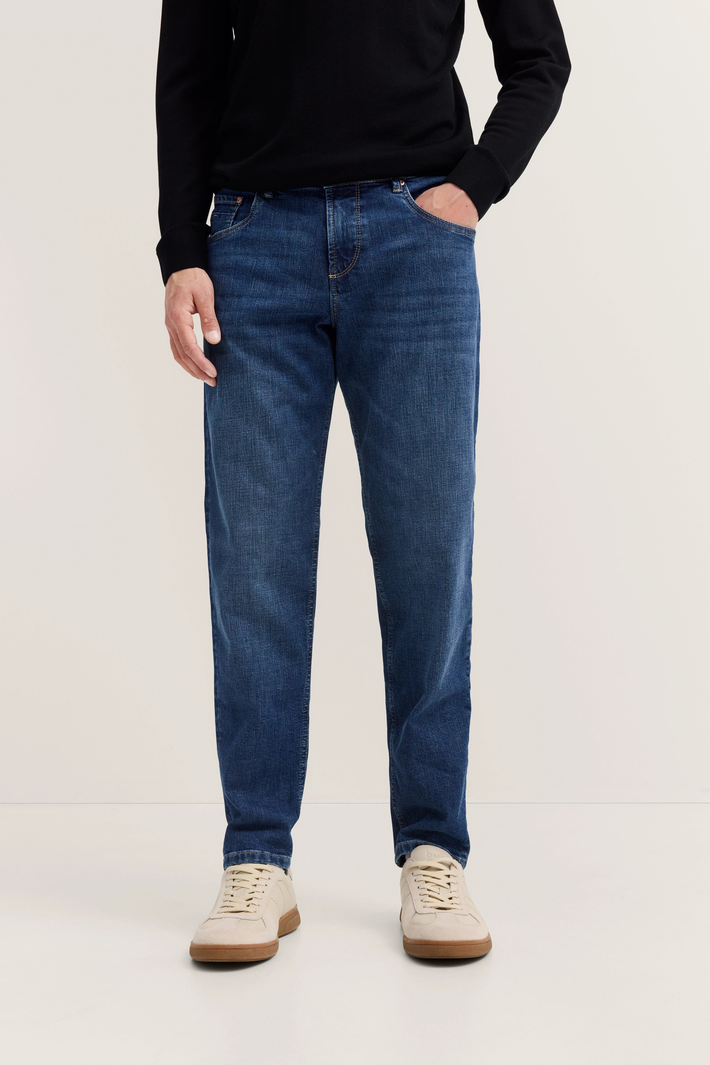 Jeans in Blau, legeres Modelbild, Hände in Taschen, schwarzer Pullover, weiße Sneaker, bugatti-Stil.