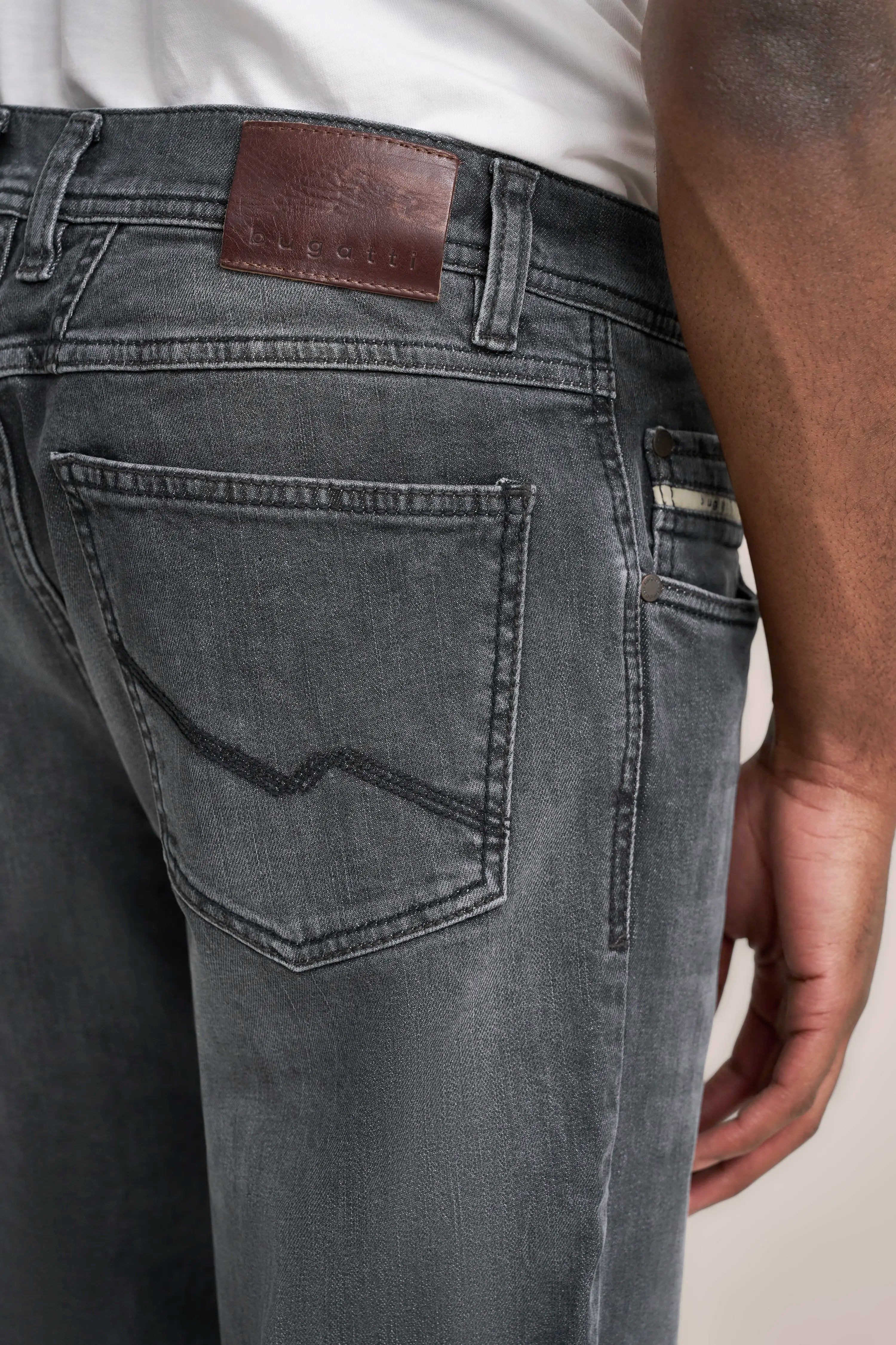 Graue bugatti Jeans in Nahaufnahme mit braunem Lederetikett, legeres Modelbild, Rückansicht.