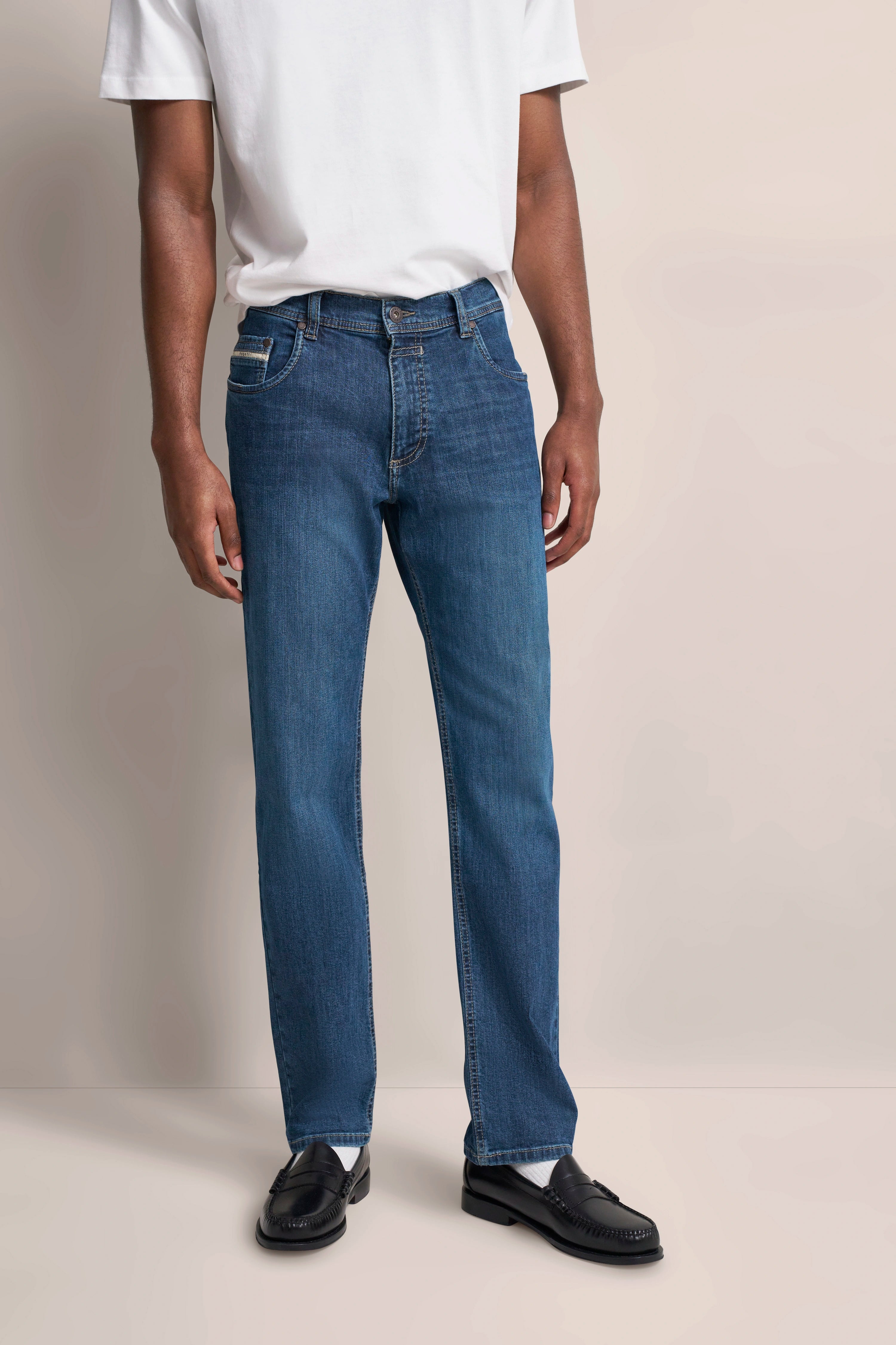 Model trägt weiße T-Shirt, blaue Jeans und schwarze Schuhe, legeres Standing.