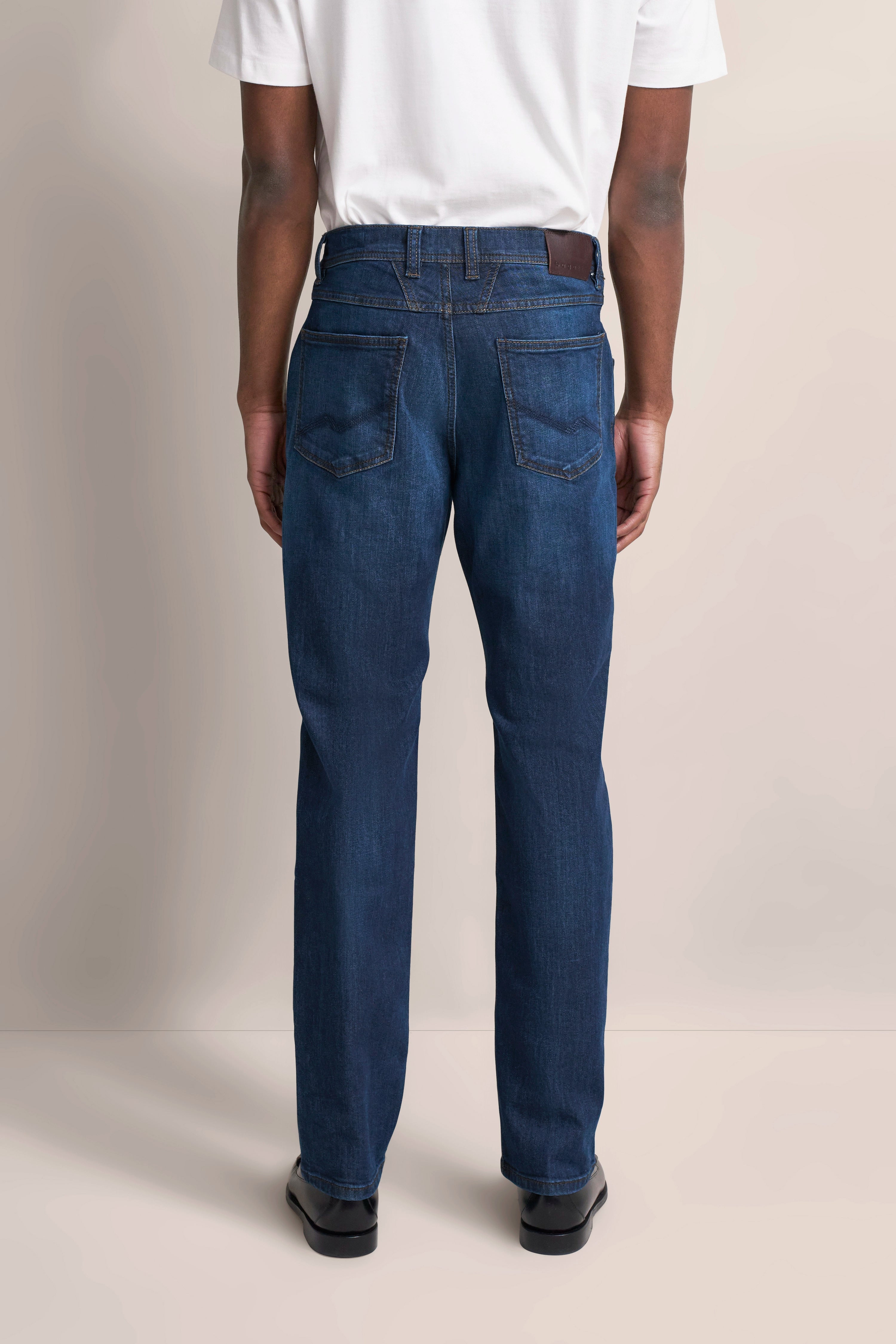 bugatti Jeans in Blau, legeres Modelbild von hinten, weißes Shirt, schwarze Schuhe.