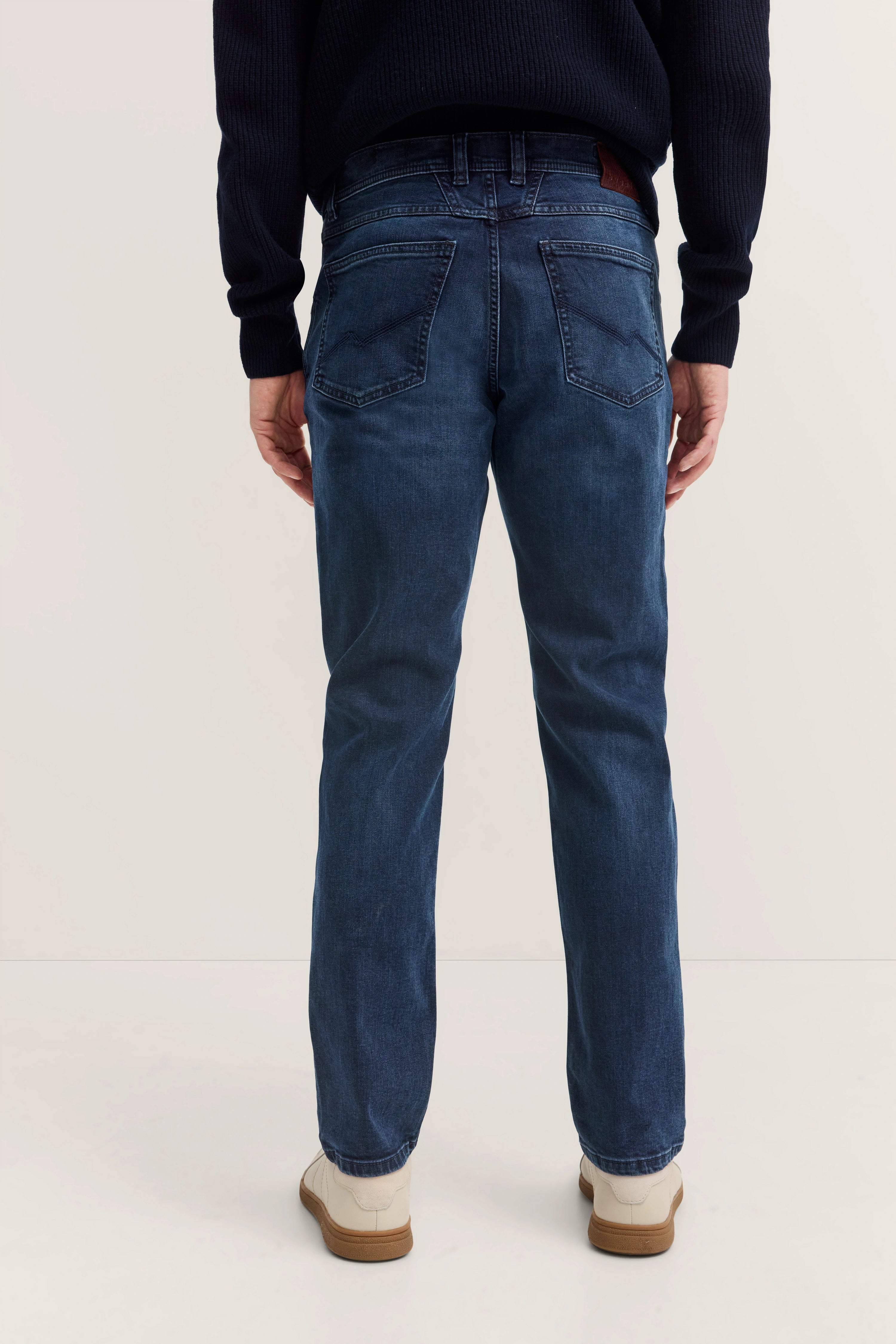 Rückansicht: Model in dunkelblauer Jeans und dunkelblauem Pullover von bugatti, weiß-braune Schuhe.