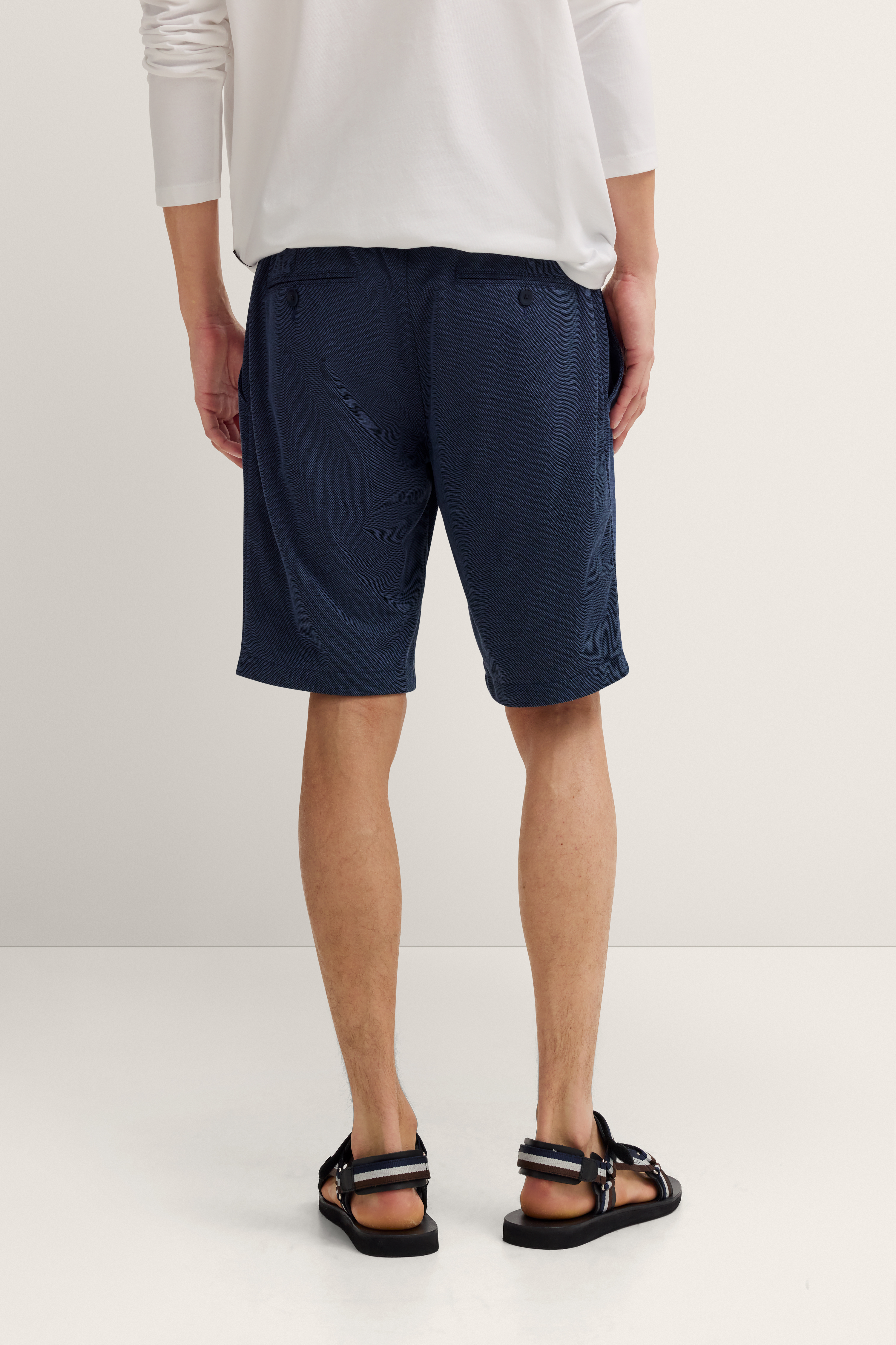 Weißes Langarmshirt und dunkelblaue Shorts von hinten, legeres Modelbild.