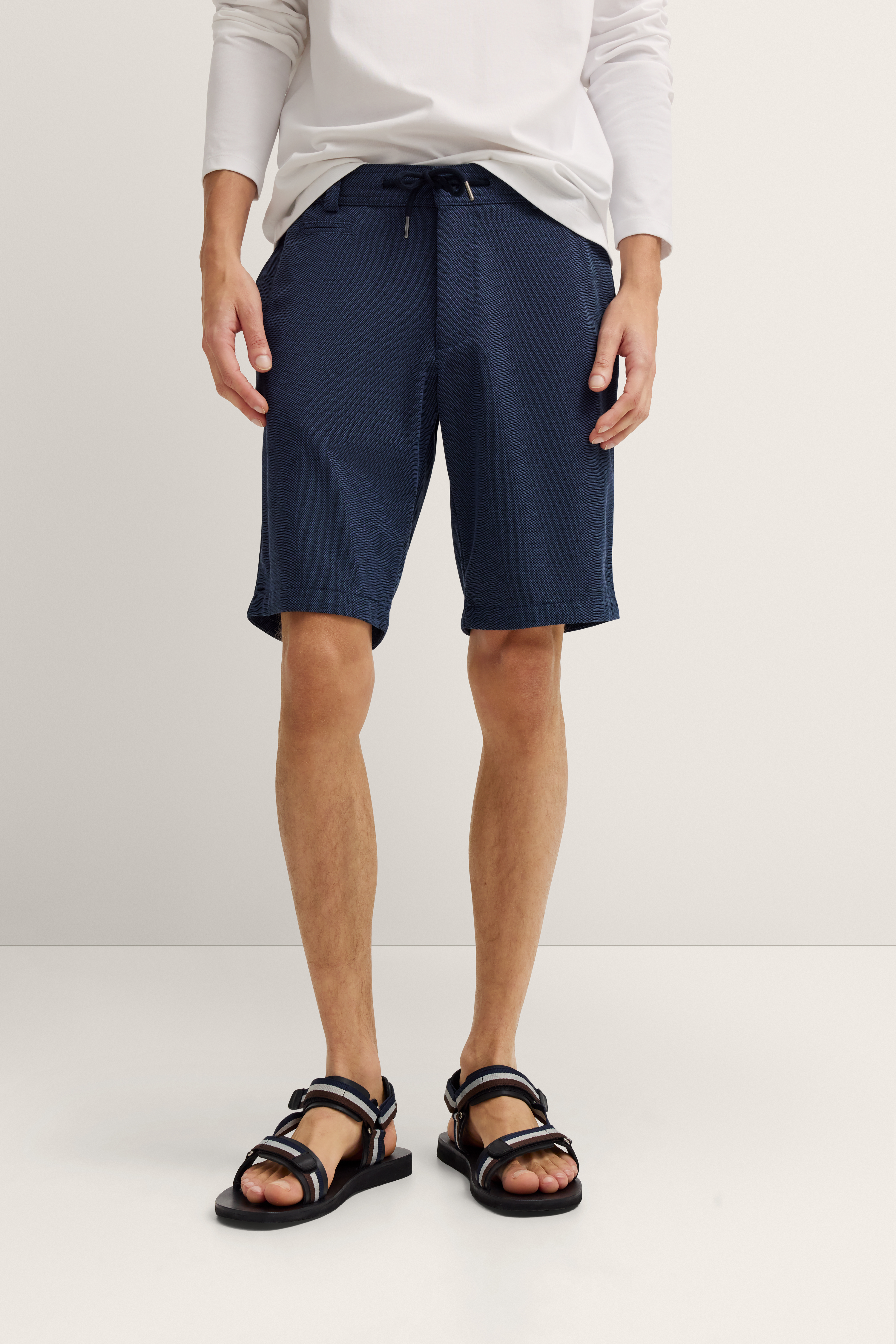 Navy Shorts und weiße Langarm-Shirt auf Model, stehend, entspannte Pose, schwarze Sandalen.