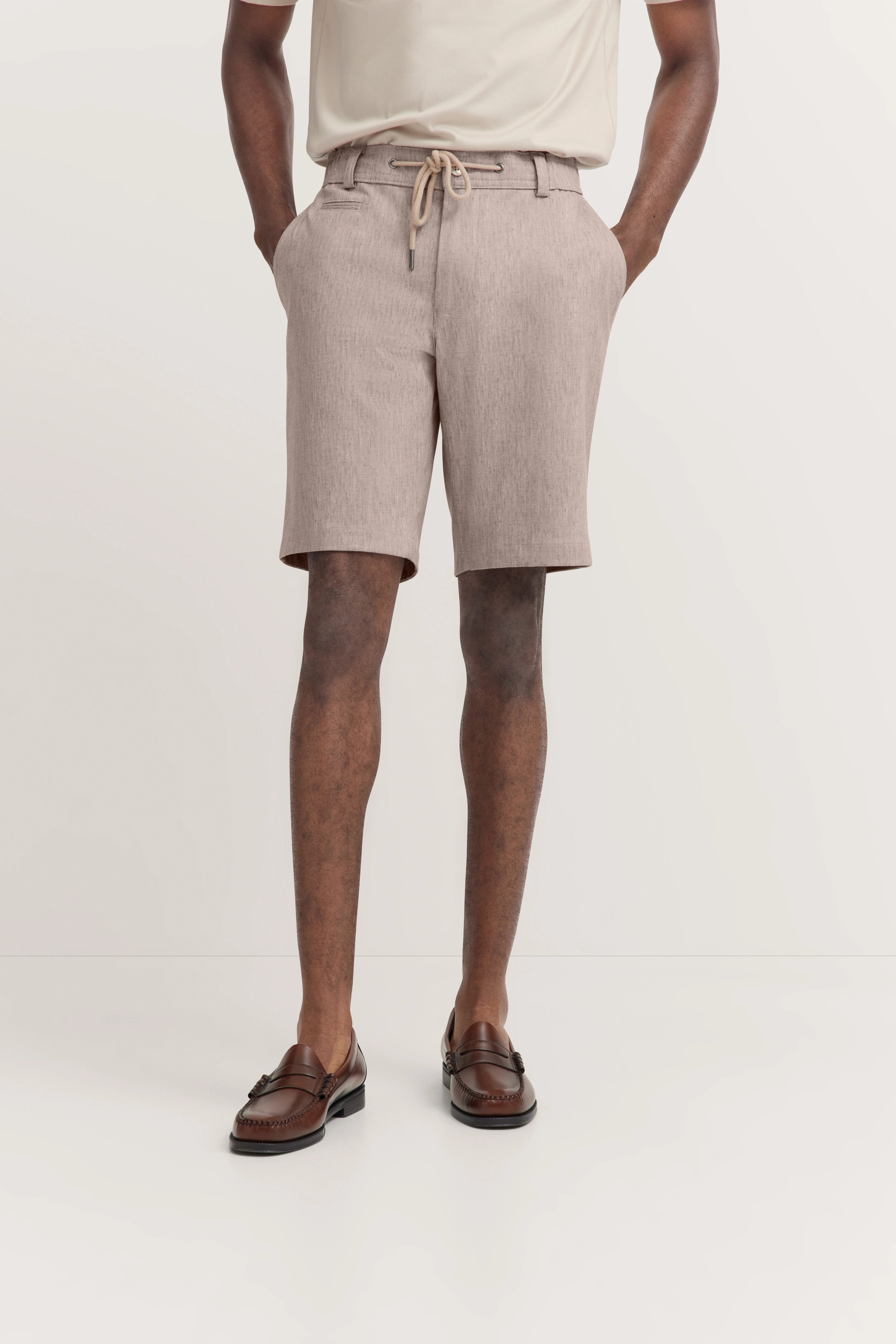Helle Shorts und cremefarbenes T-Shirt, braune Loafer, legeres Modelbild, Hände in den Taschen.