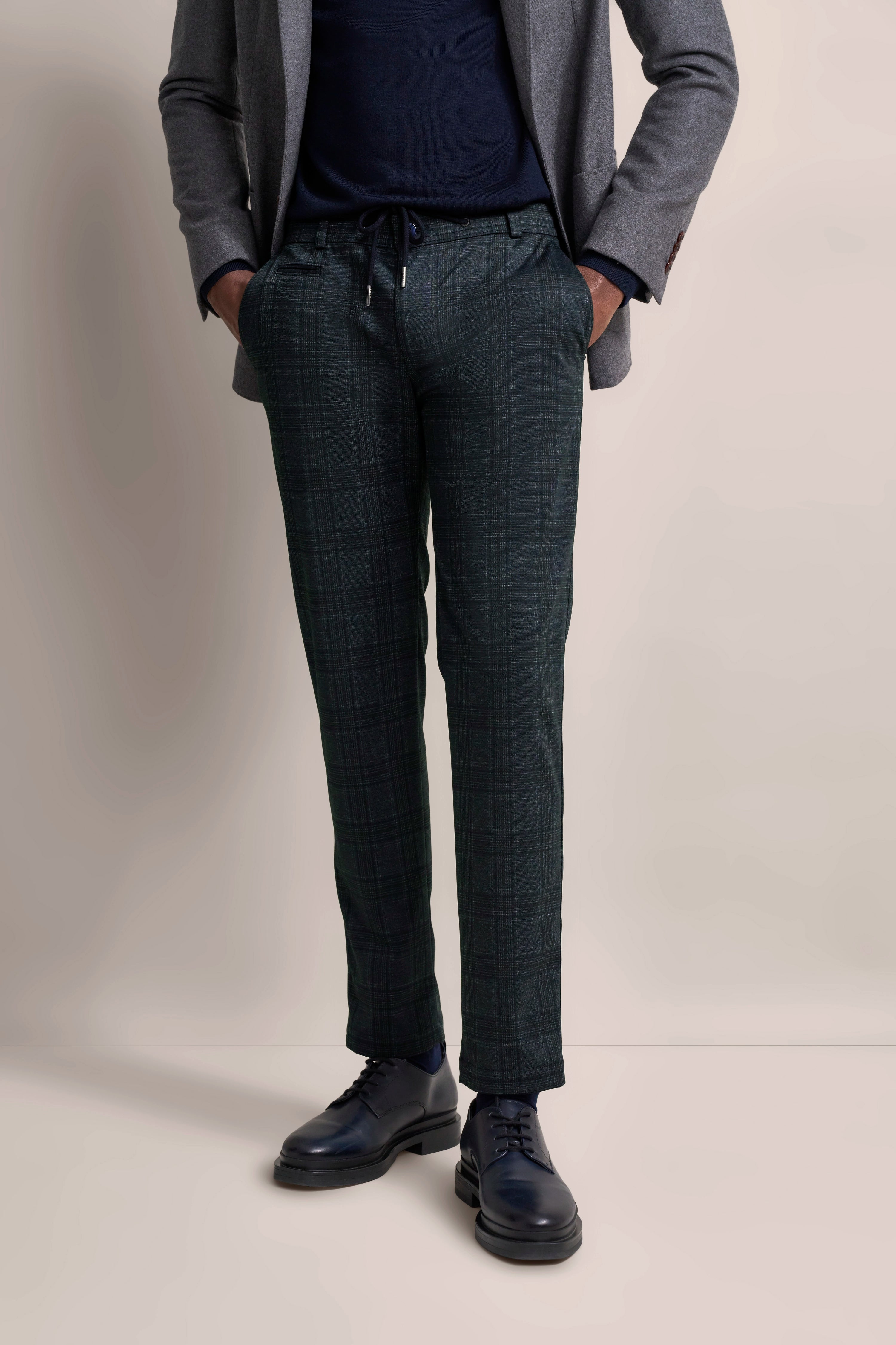Grauer Blazer und karierte Hose in Dunkelgrün, legeres Modelbild, Hände in den Hosentaschen.