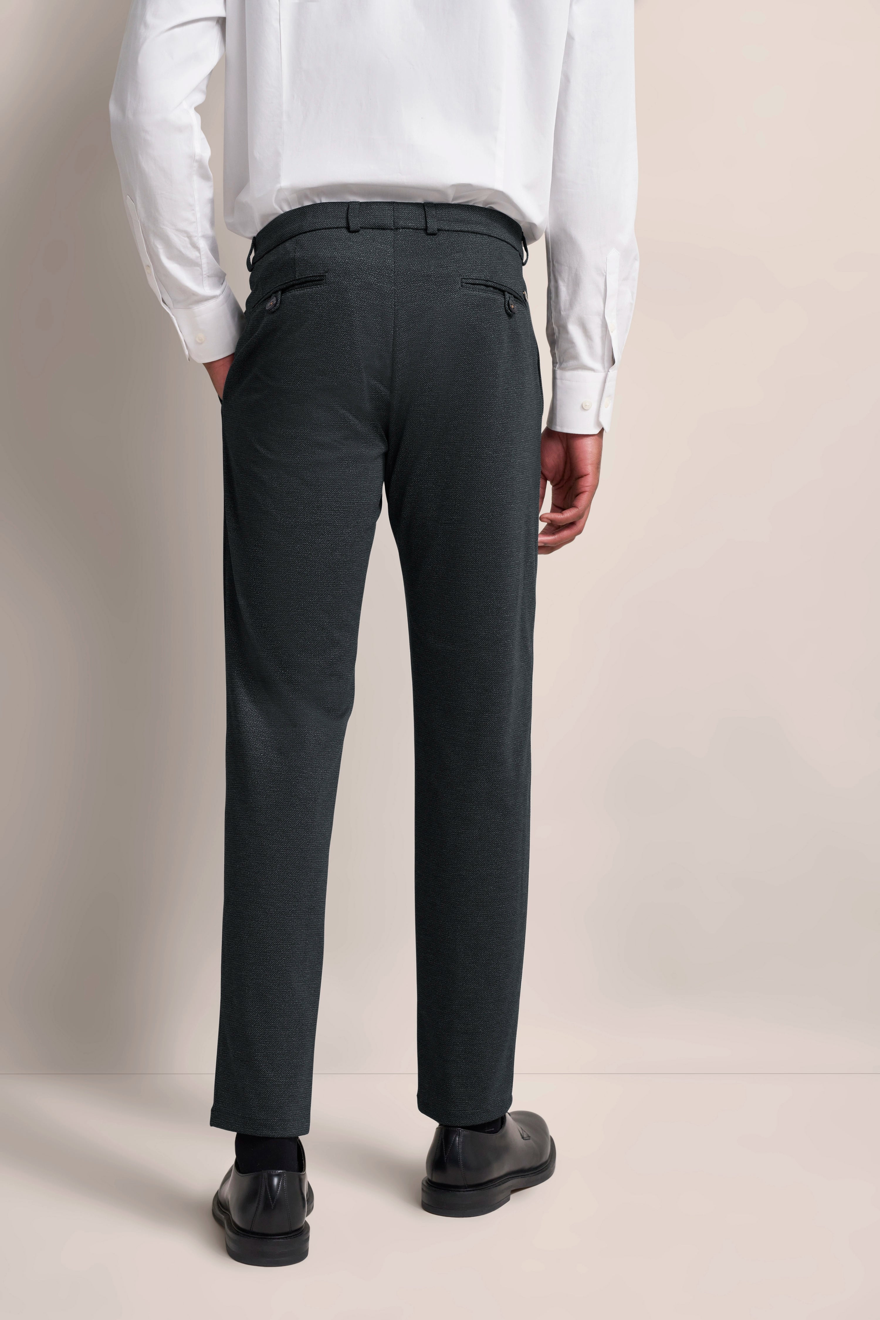 Rückansicht eines Models in schwarzer Hose und weißem Hemd, legeres Posing, bugatti Stil.