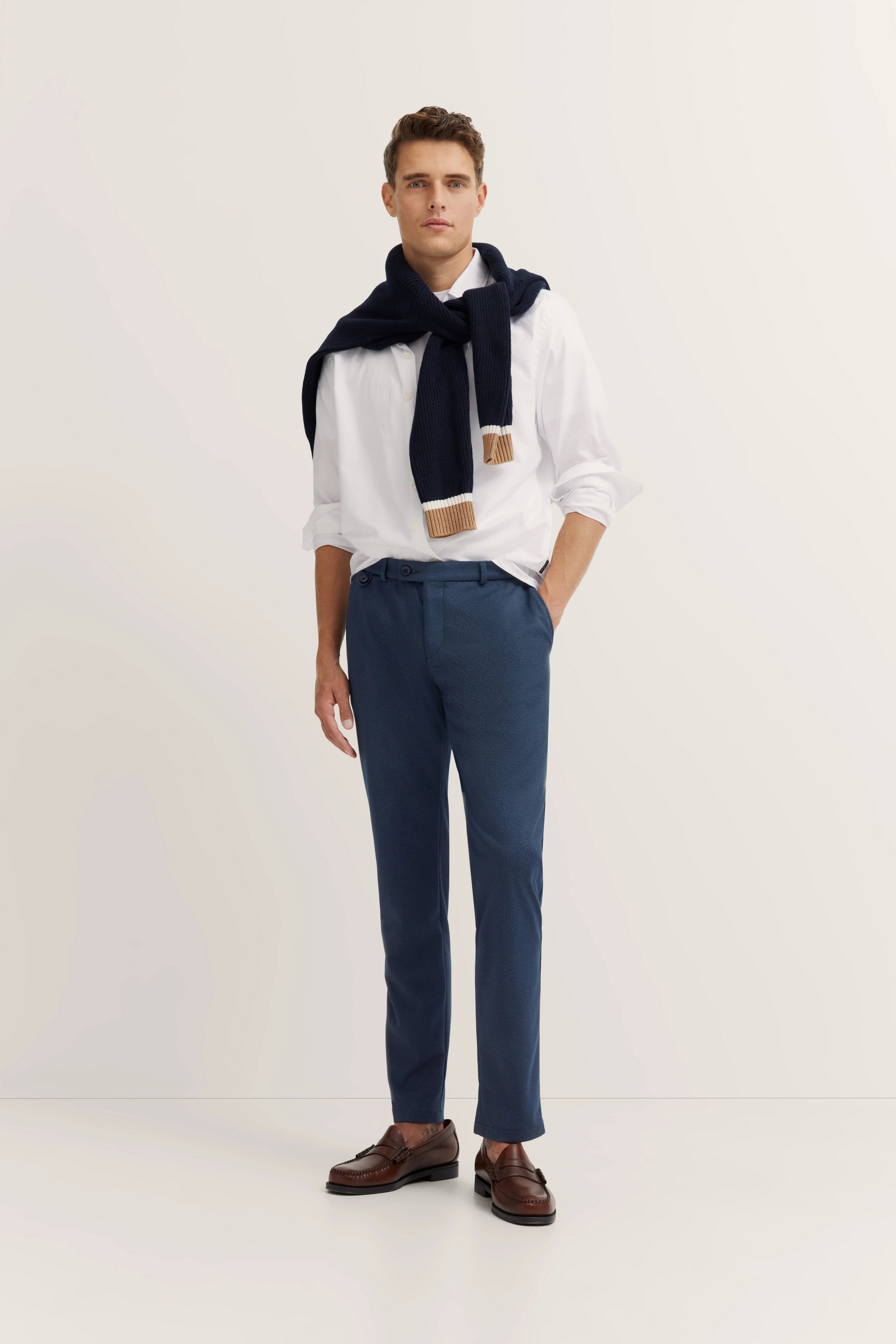 Model in wit overhemd, blauwe broek, bruine schoenen, straalt bugatti's tijdloze elegantie en Italiaanse flair uit.