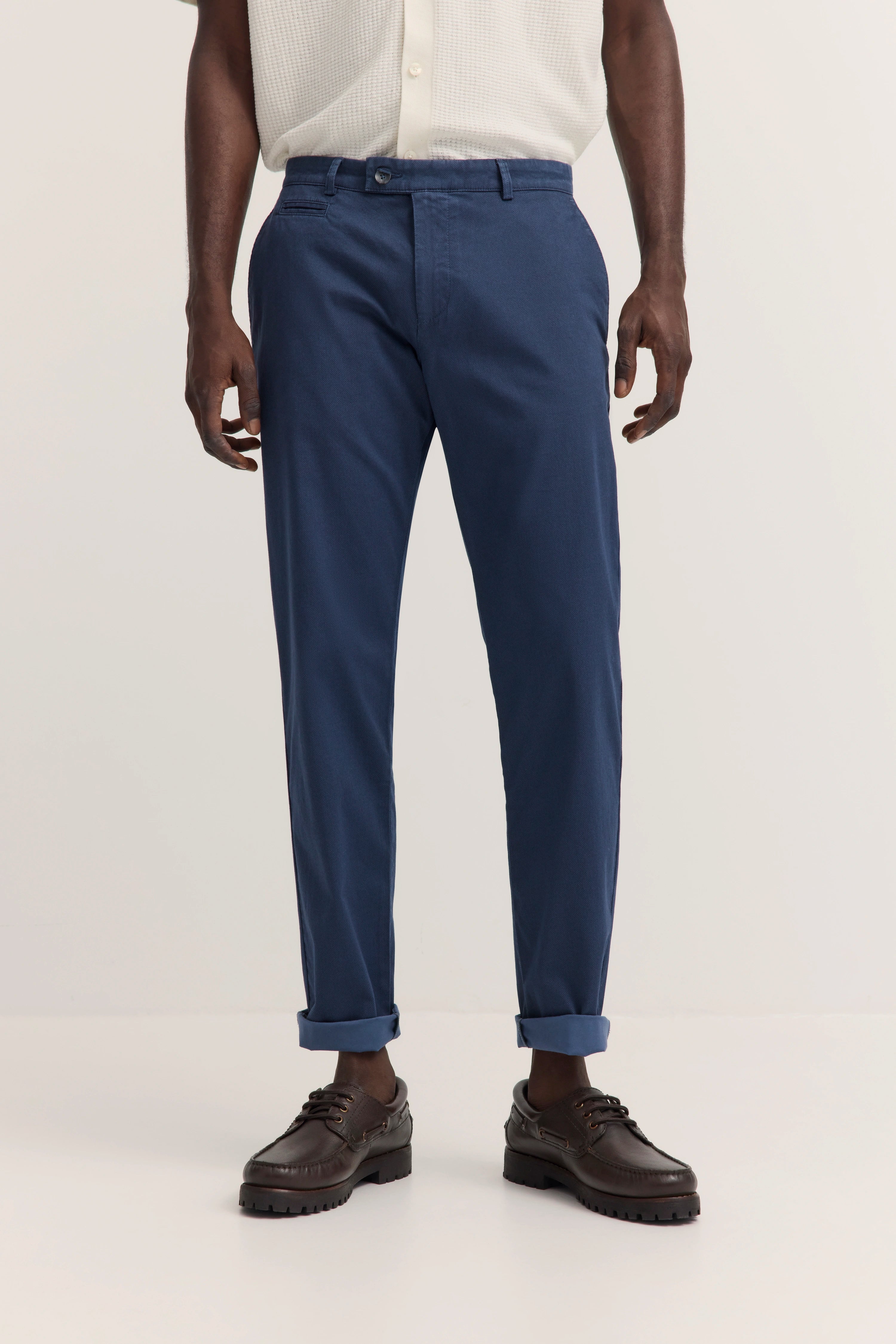 Blaues Chino-Outfit mit weißem Hemd und braunen Schuhen. Legeres Modelbild, entspannter Stand.