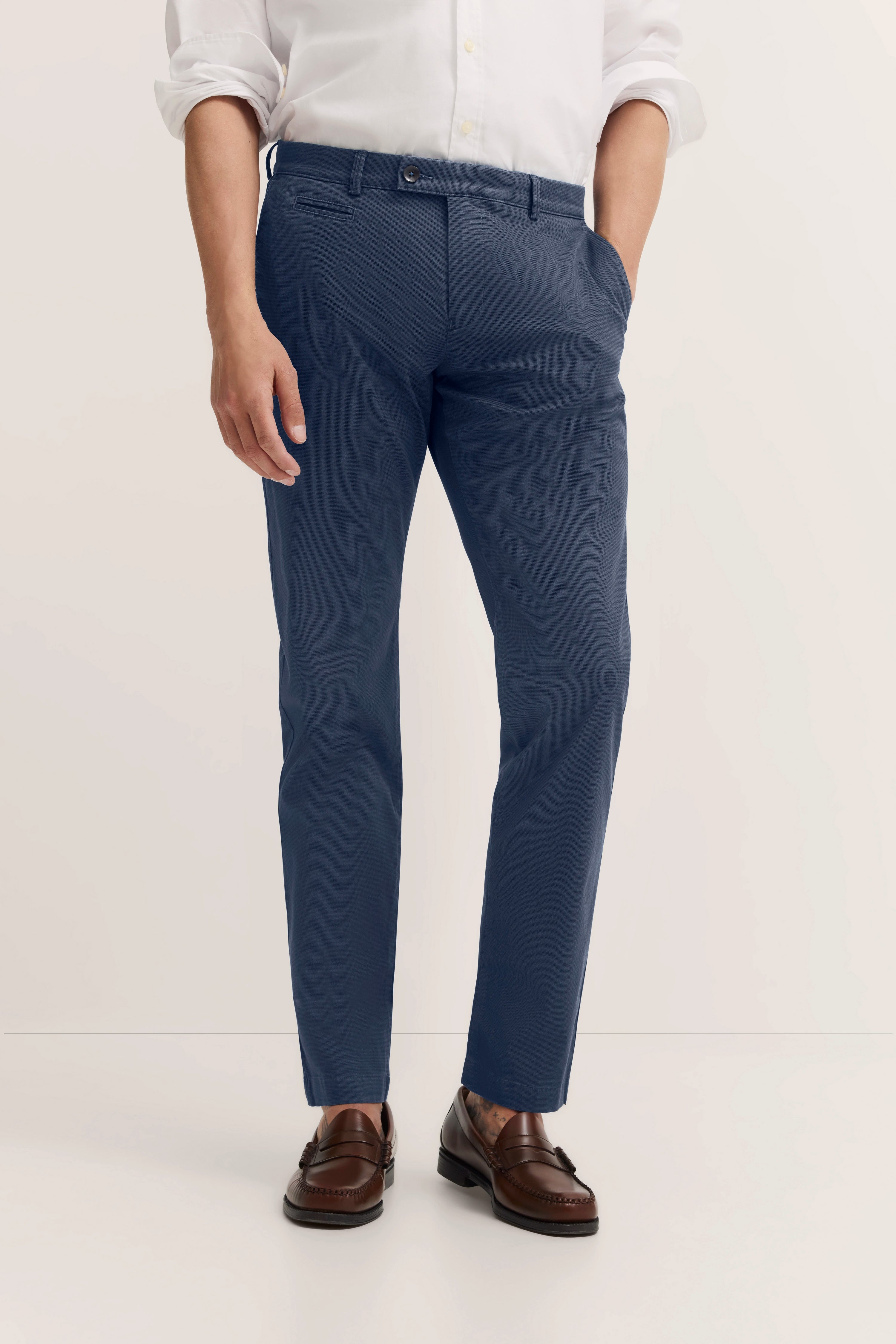 Weiße Hemd und blaue Hose, legeres Modelbild, Hände in Taschen, braune Schuhe.