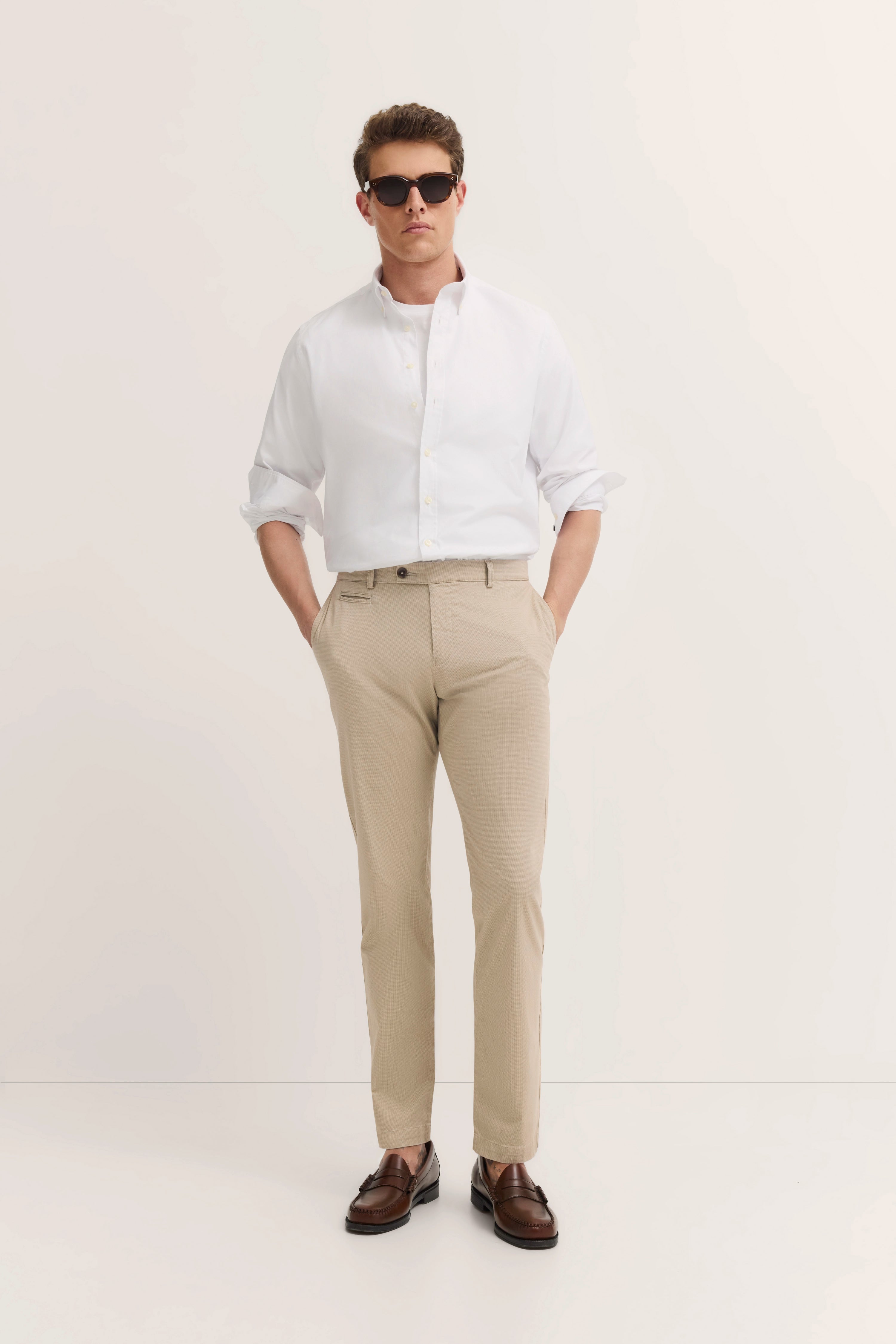Weißes Hemd und beige Hose, braune Schuhe, Model stehend mit Händen in den Taschen.