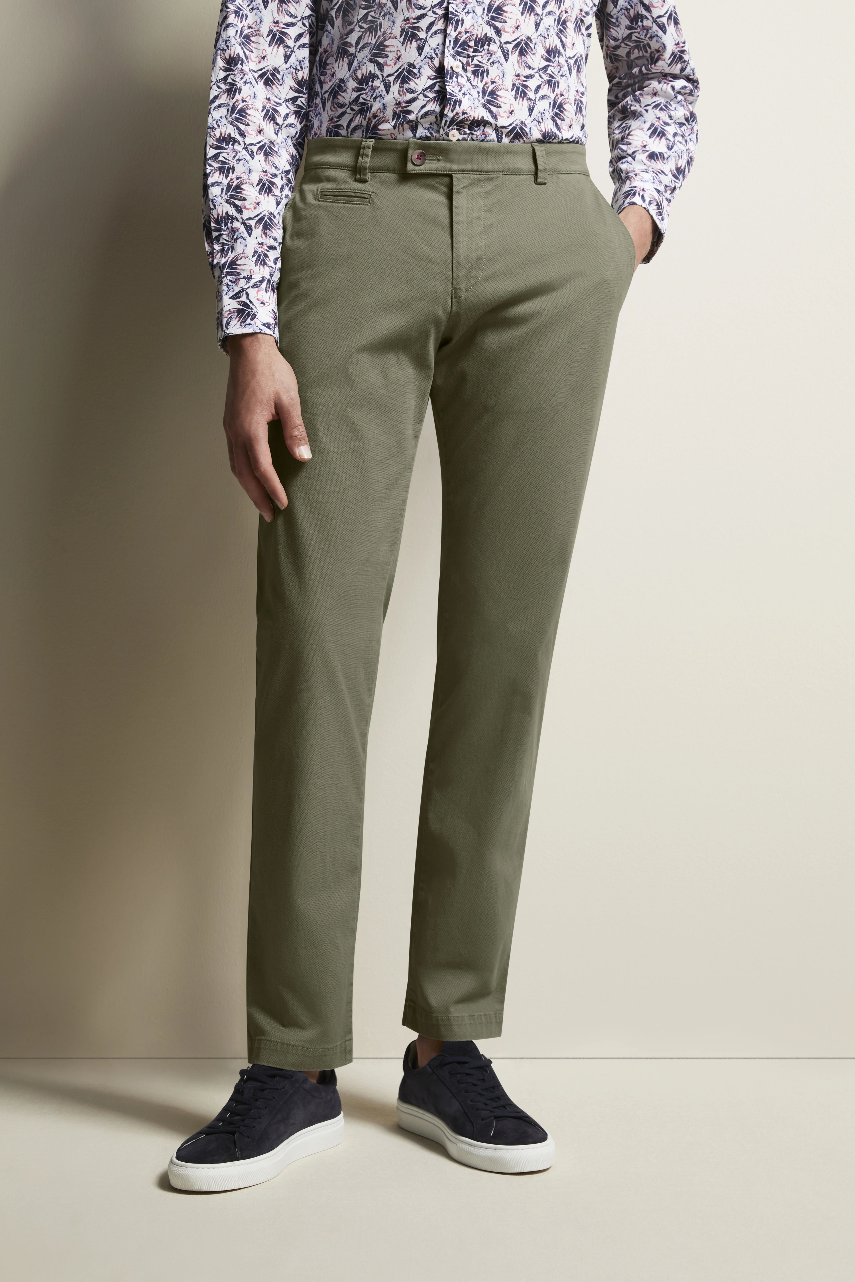 Model in groene chino, bloemig shirt, donkere sneakers, ontspannen pose.