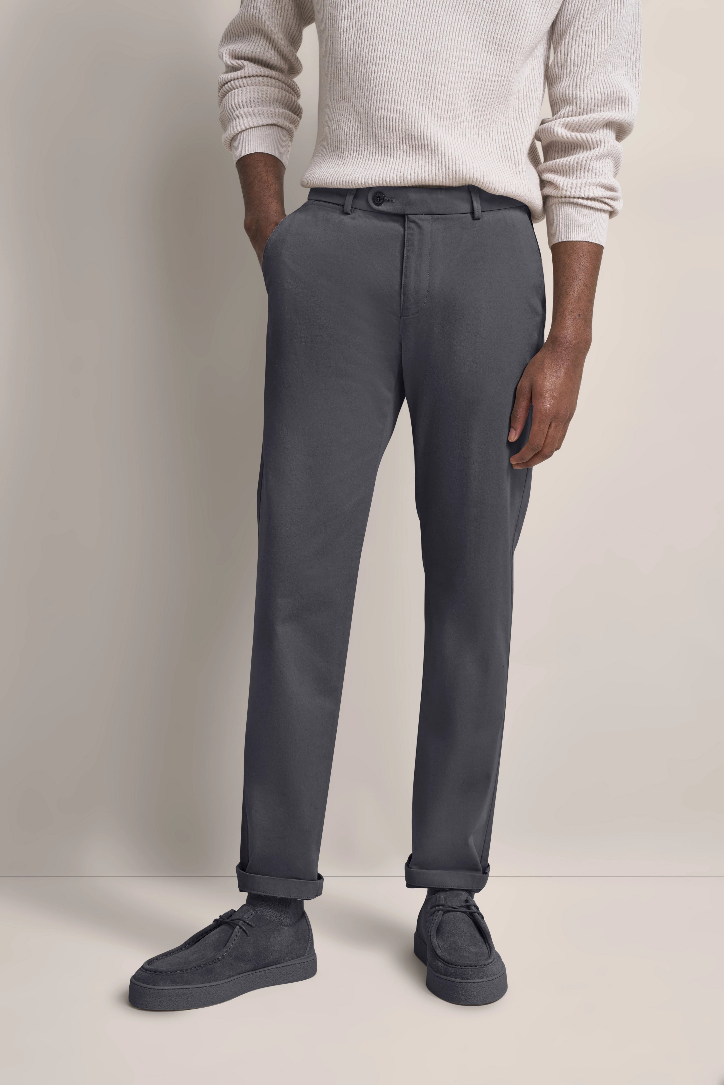 Graue Chinos mit weißem Strickpullover, legeres Modelbild, Hände in Taschen.