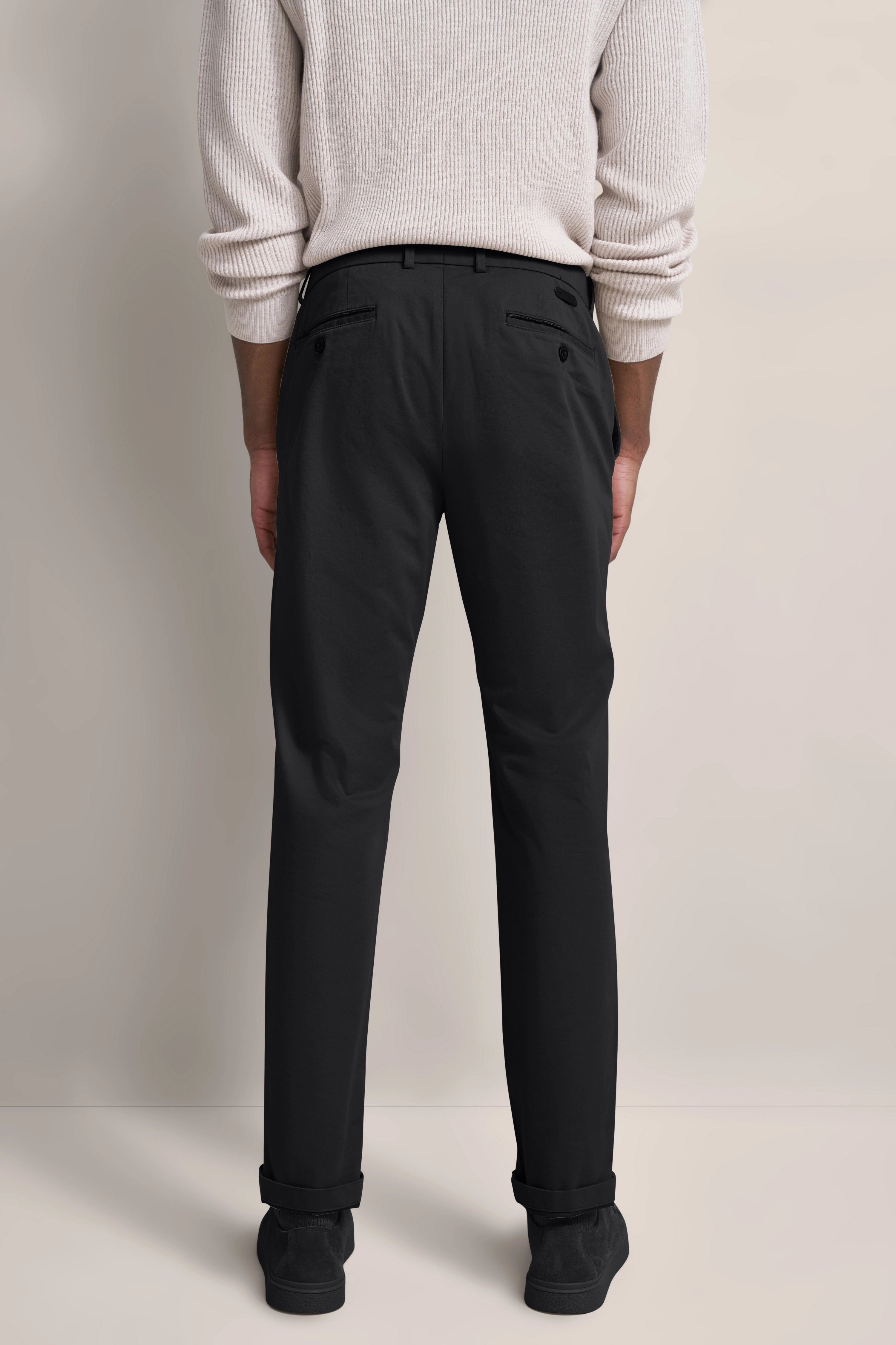 Rückansicht Model in schwarzer Hose und cremefarbenem Pullover, lässig stehend.
