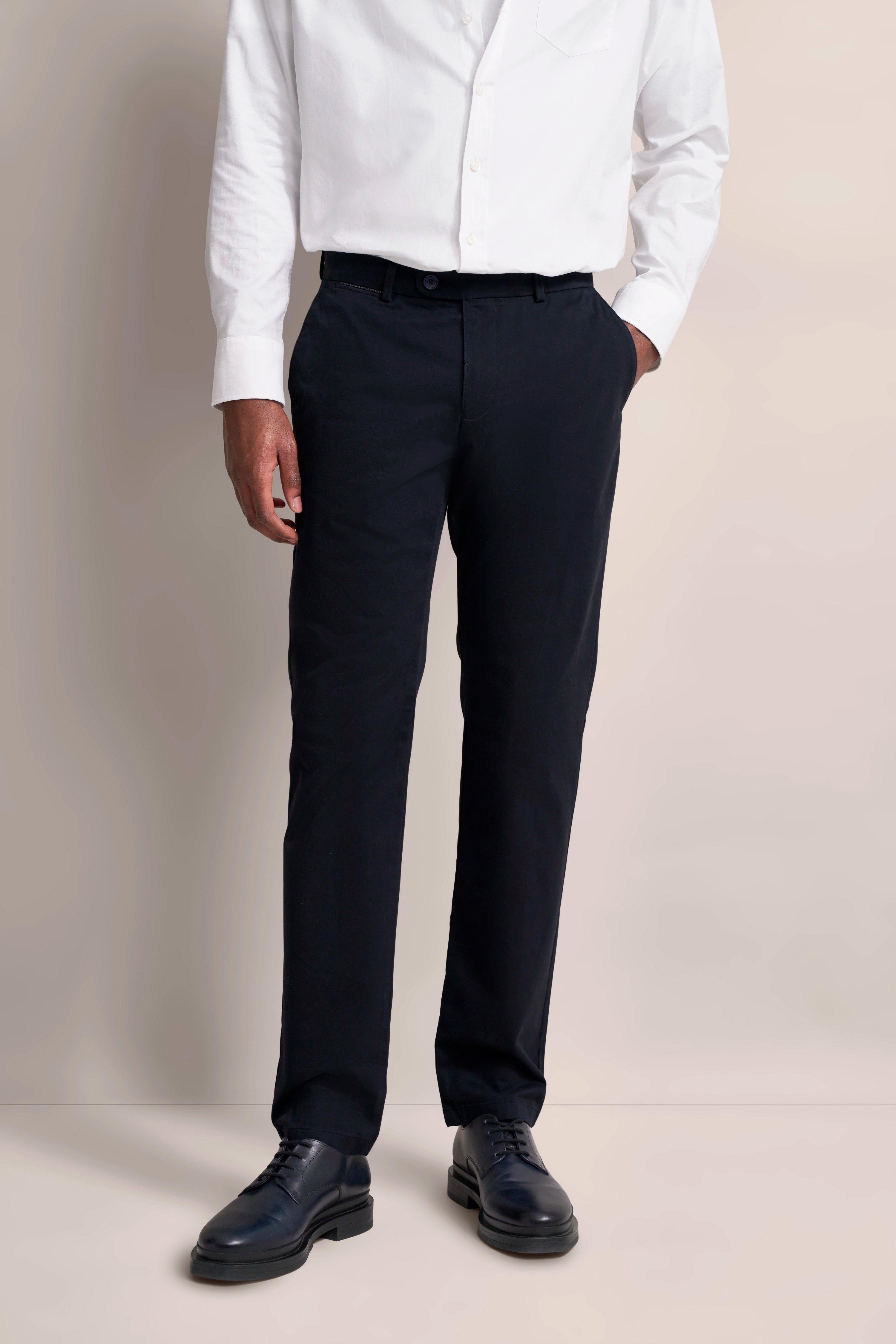 Weißes Hemd mit dunkelblauer Hose, legeres Modelbild, Hände in Taschen.