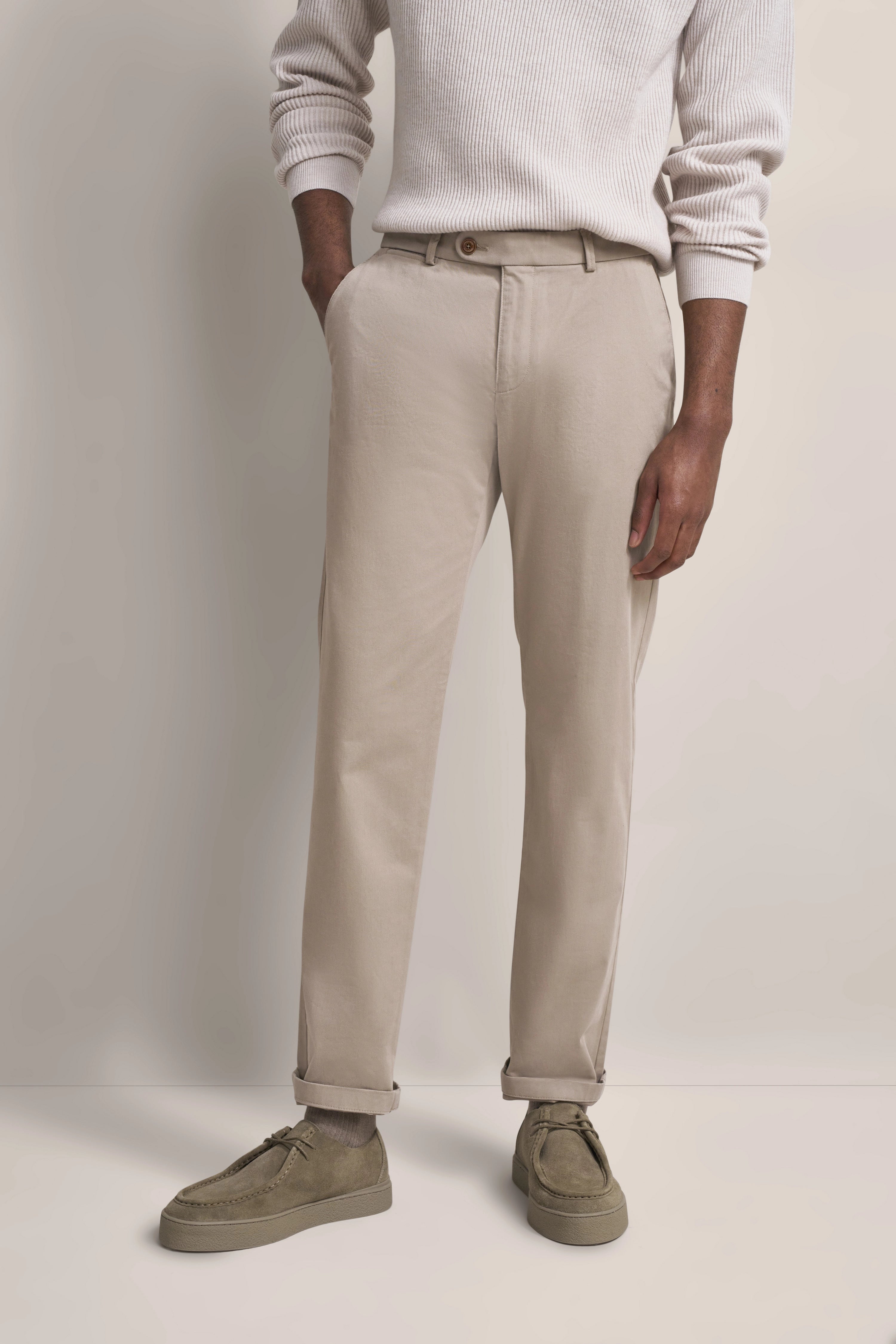 Beiger Pullover und Chinos, legeres Modelbild, Hände in Taschen, Stil von bugatti.