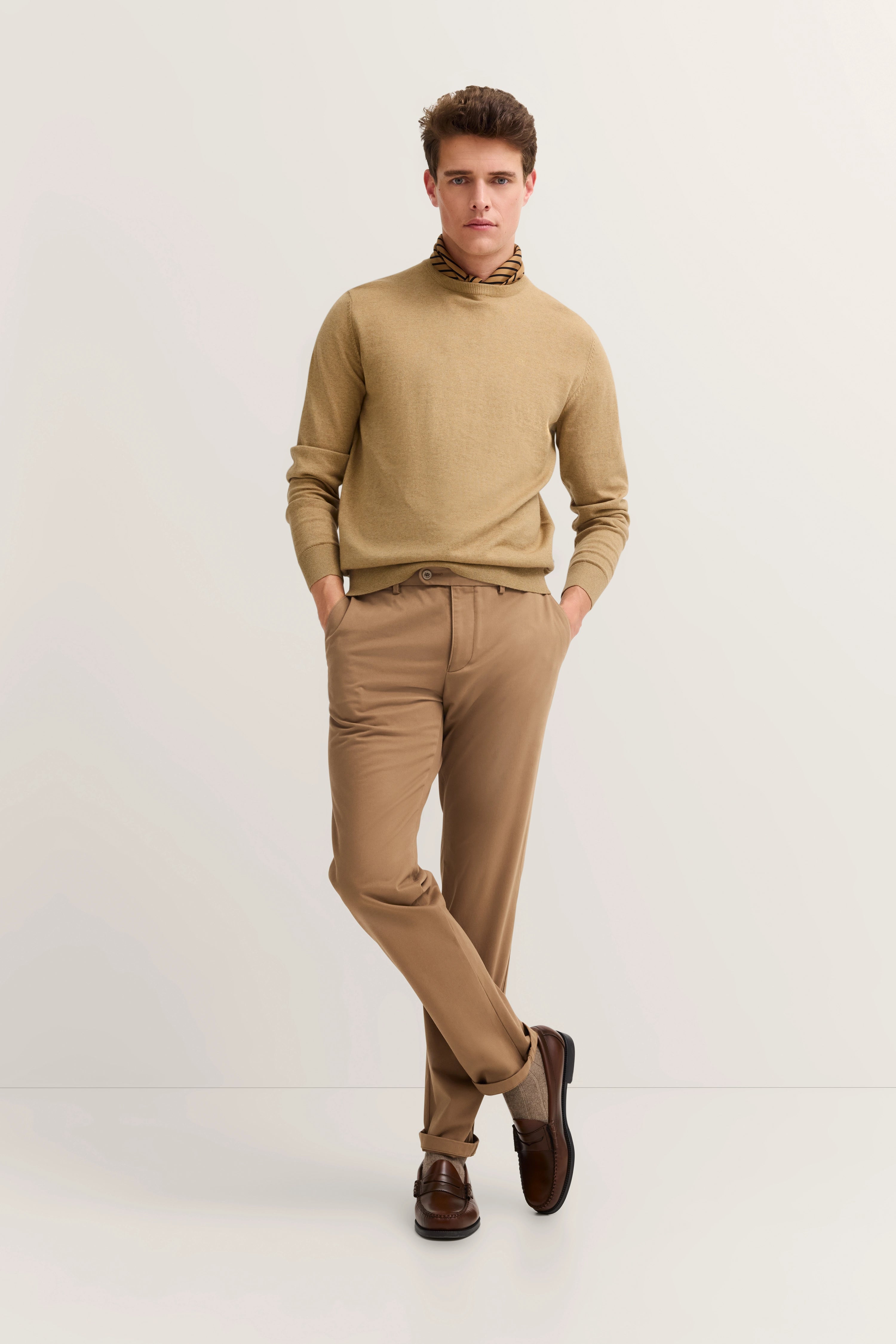 Beiger Rollkragenpullover und braune Hose von bugatti, Model stehend mit Händen in Hosentaschen.