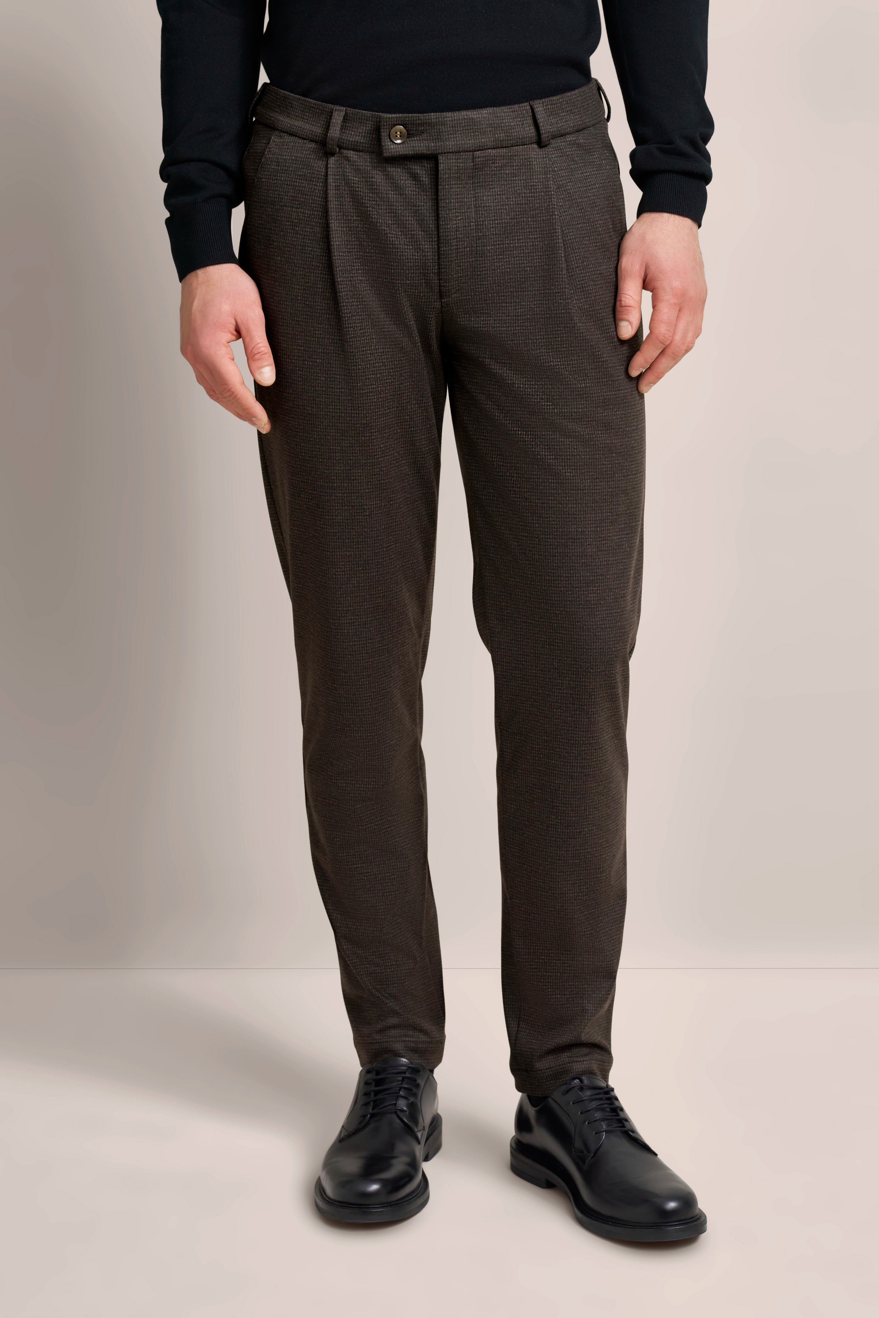 bugatti Legerbild: Schwarzer Pullover, braune Hose, schwarze Schuhe, entspannter Stand.
