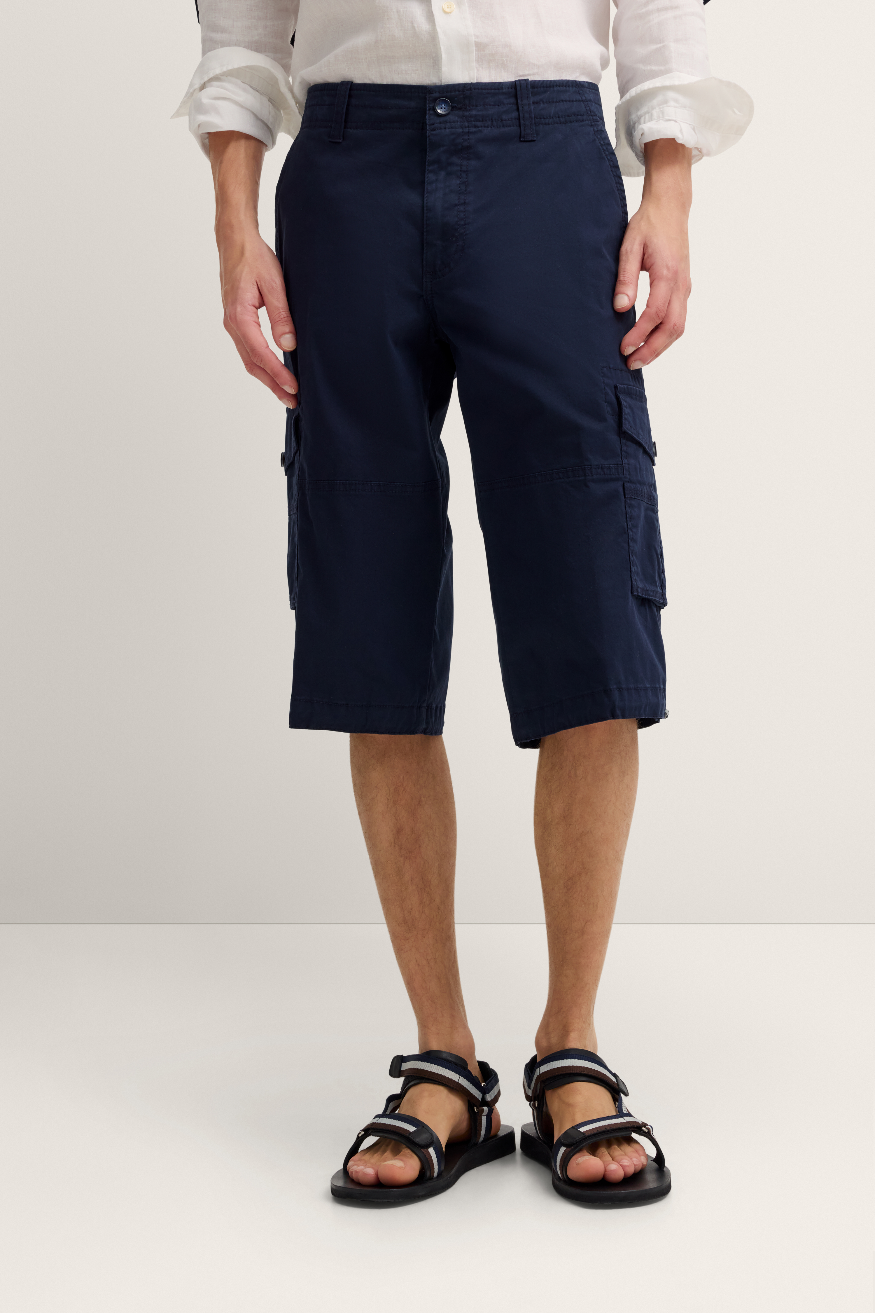 Navy Cargo-Bermuda mit weißem Hemd und Sandalen, legeres Modelbild, entspannte Pose.