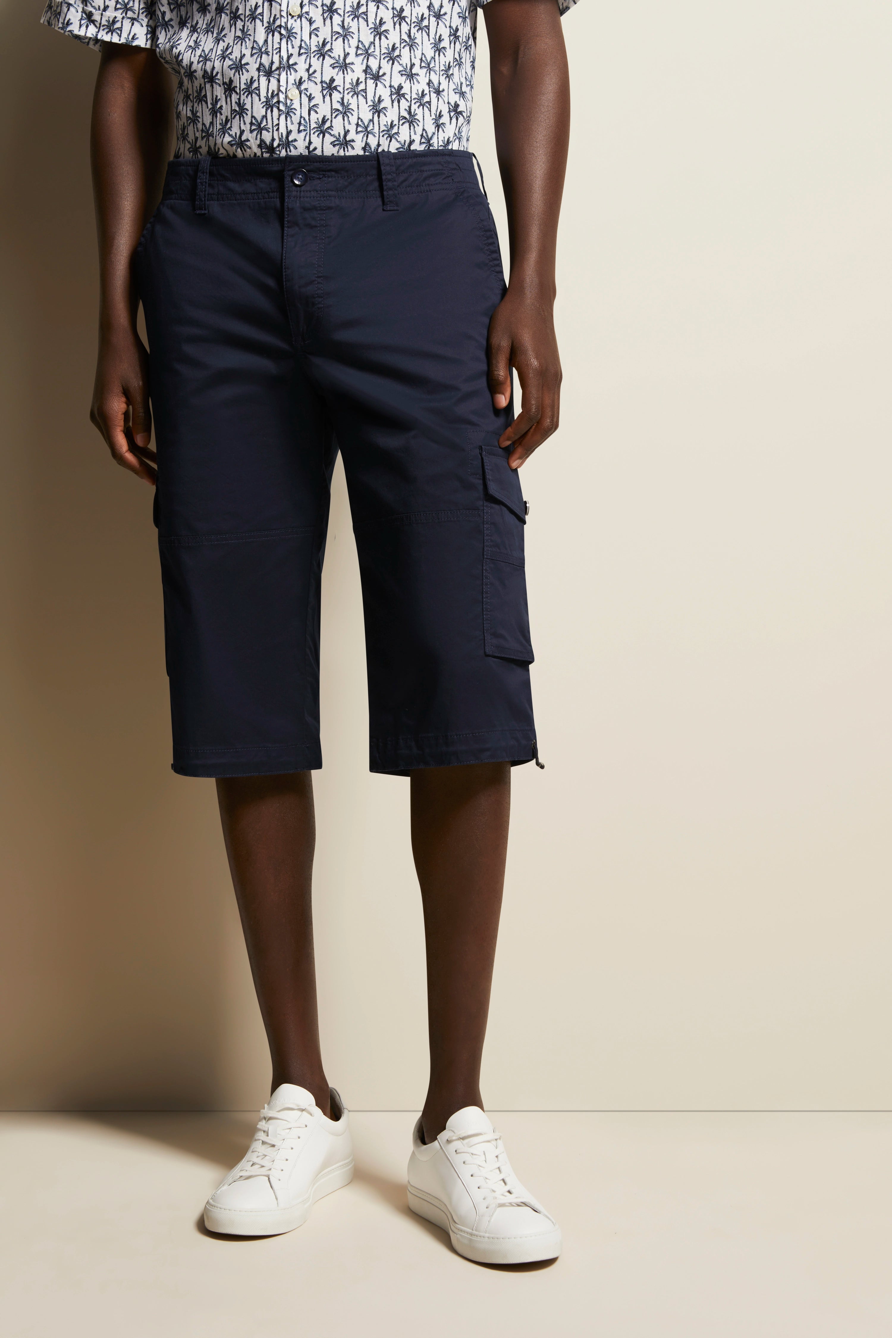 Donkerblauwe cargoshorts met palmenhemd, witte sneakers, casual model, staande pose.
