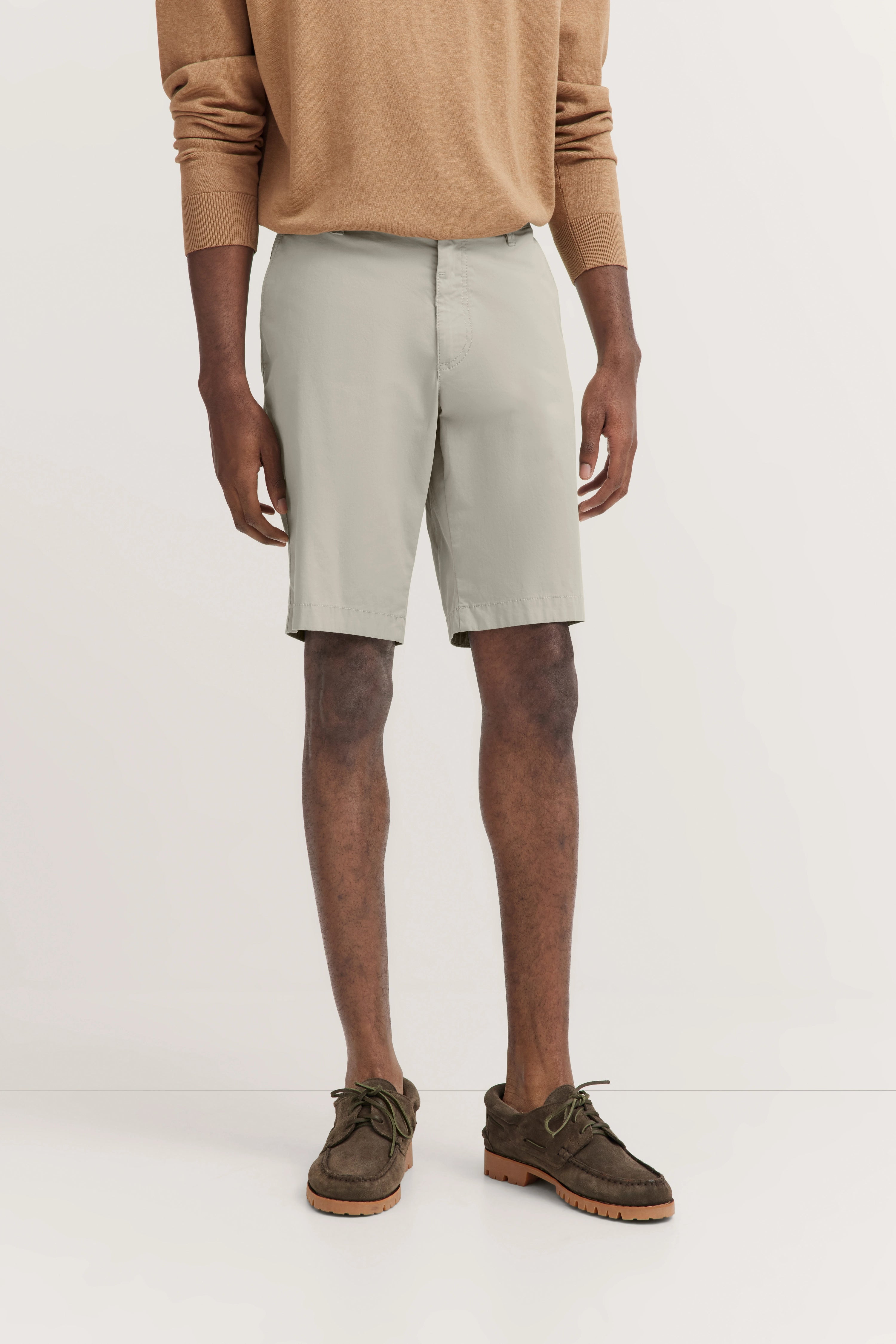 Beige Pullover und helle Shorts, legeres Modelbild, entspannte Haltung.
